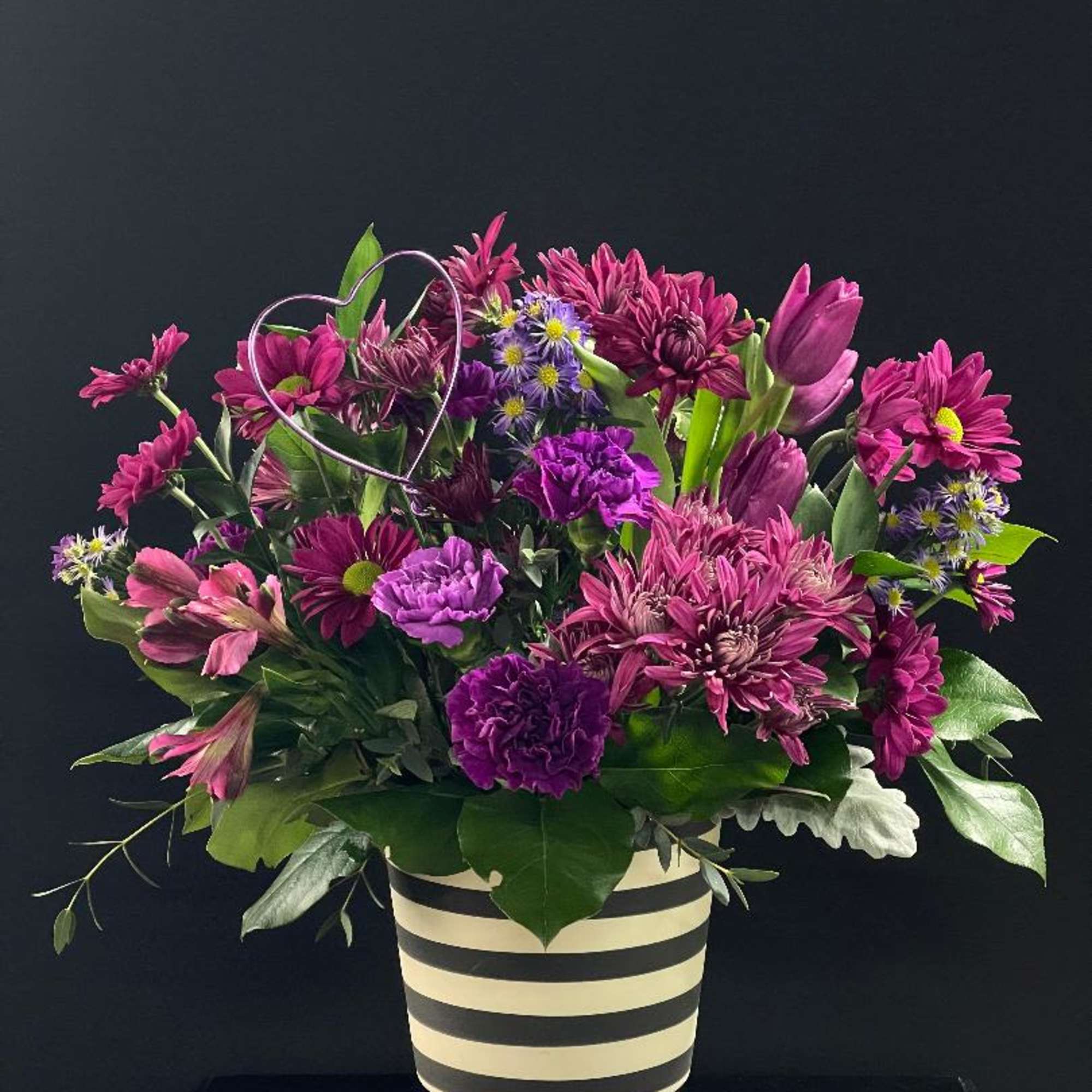 Purple and pink mixed bouquet in a striped vase with a wire heart accent