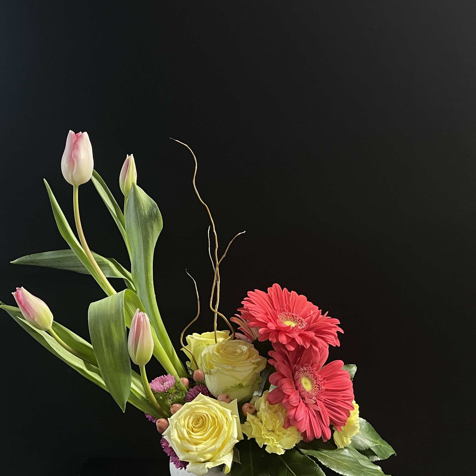 Pink tulips and yellow roses with bright pink gerbera daisies in a white vase.