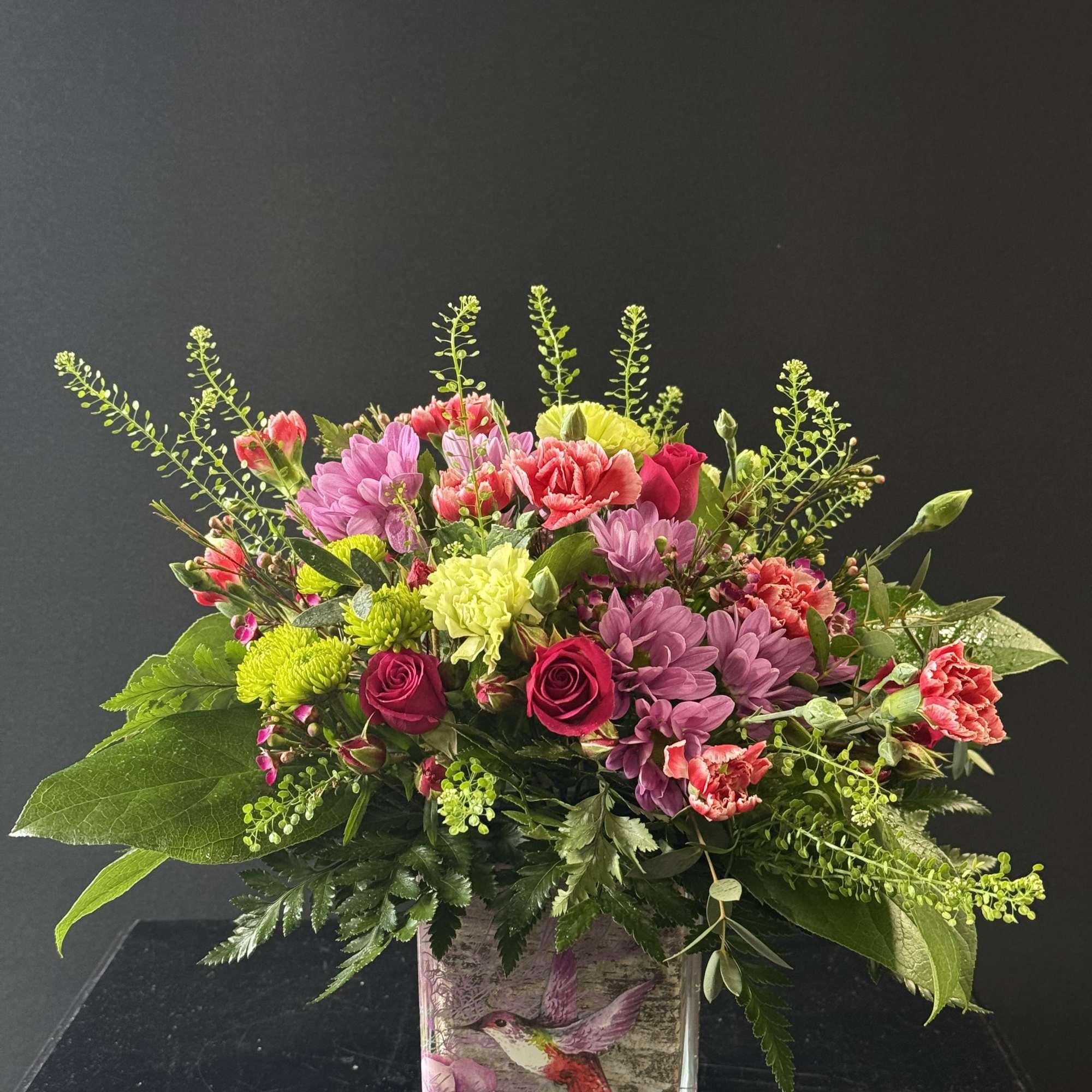 Mixed bouquet of pink, purple, and green flowers in a glass vase