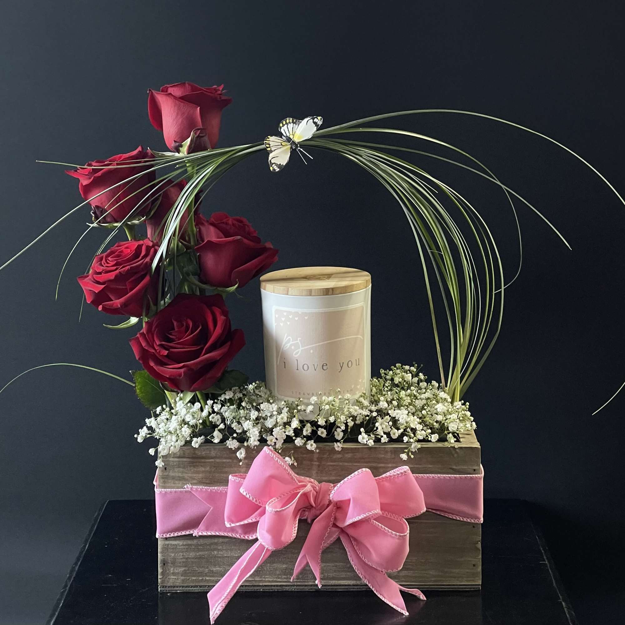 Red roses arranged with a candle in a wooden box and pink ribbon
