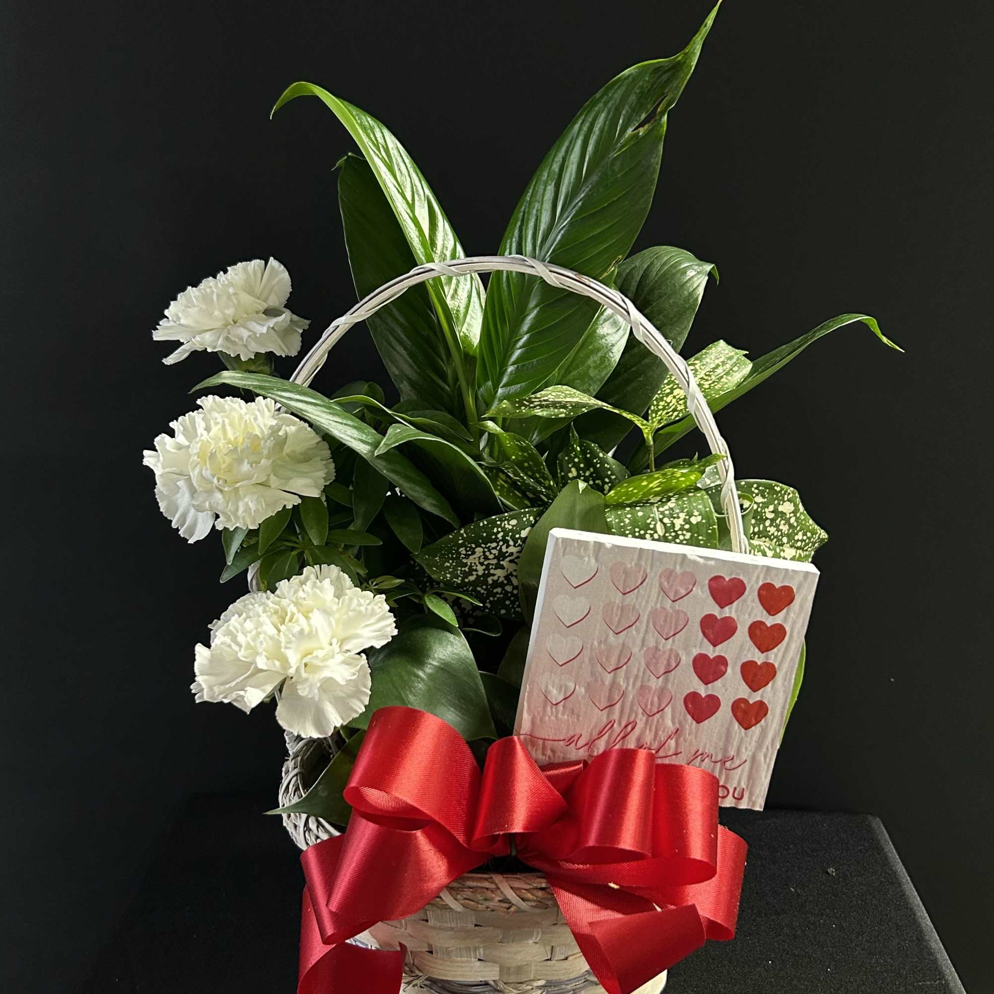 White carnations in a basket with a red bow and a heart card