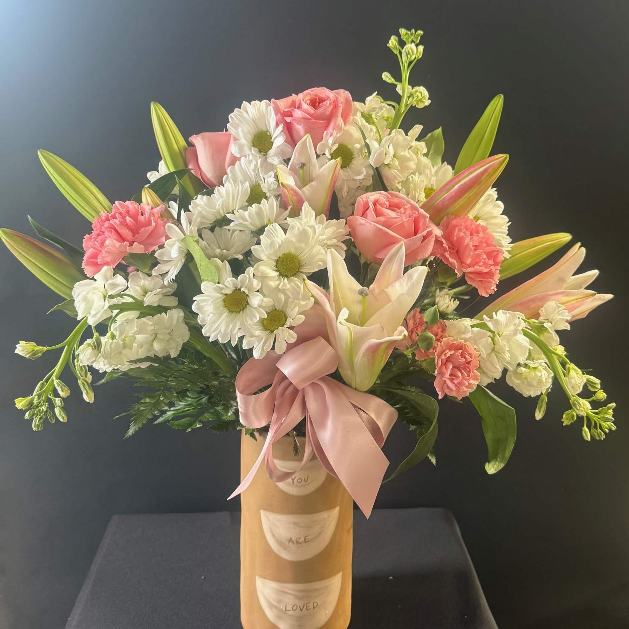 Pink roses and white daisies in a tall vase with a pink ribbon