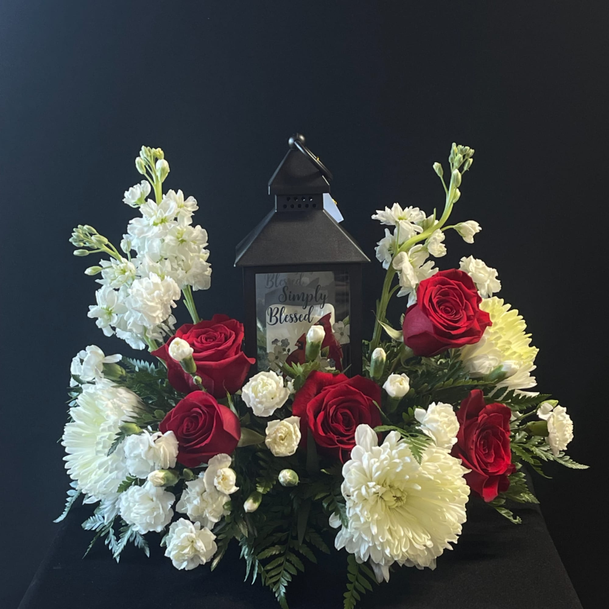 Red roses and white flowers arranged around a black lantern
