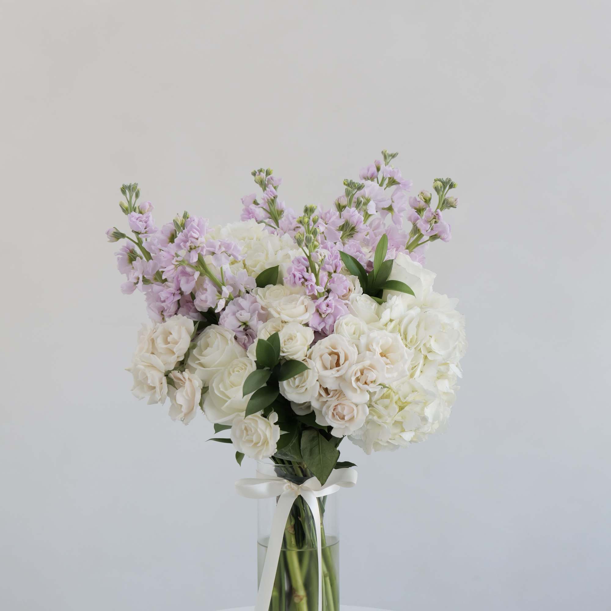 White and blush bouquet in a clear glass vase with a ribbon
