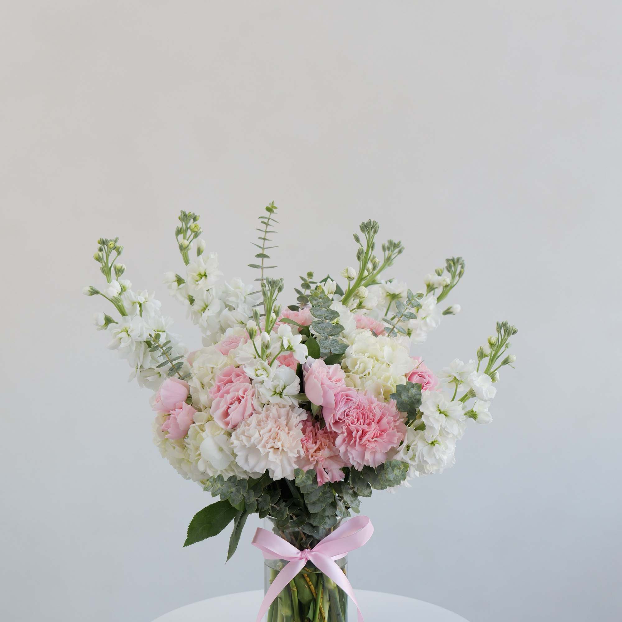 Pink and white bouquet in a clear glass vase with a pink ribbon