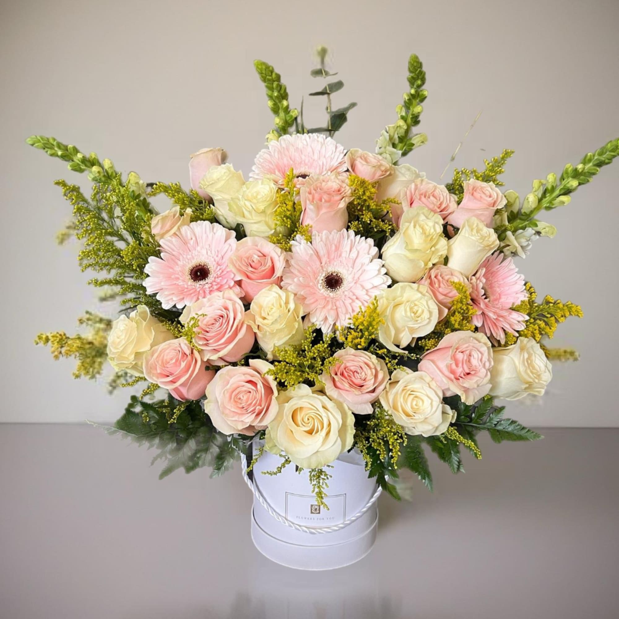 Pink and cream roses with pale pink daisies in a white hatbox