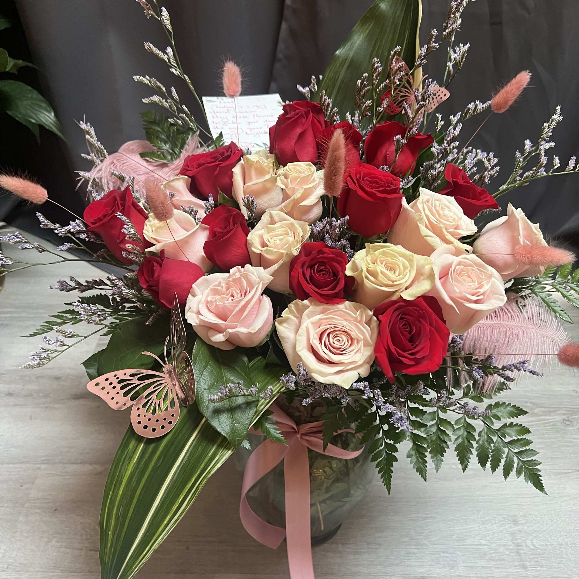 Bouquet of red and blush roses in a glass vase with pink ribbon