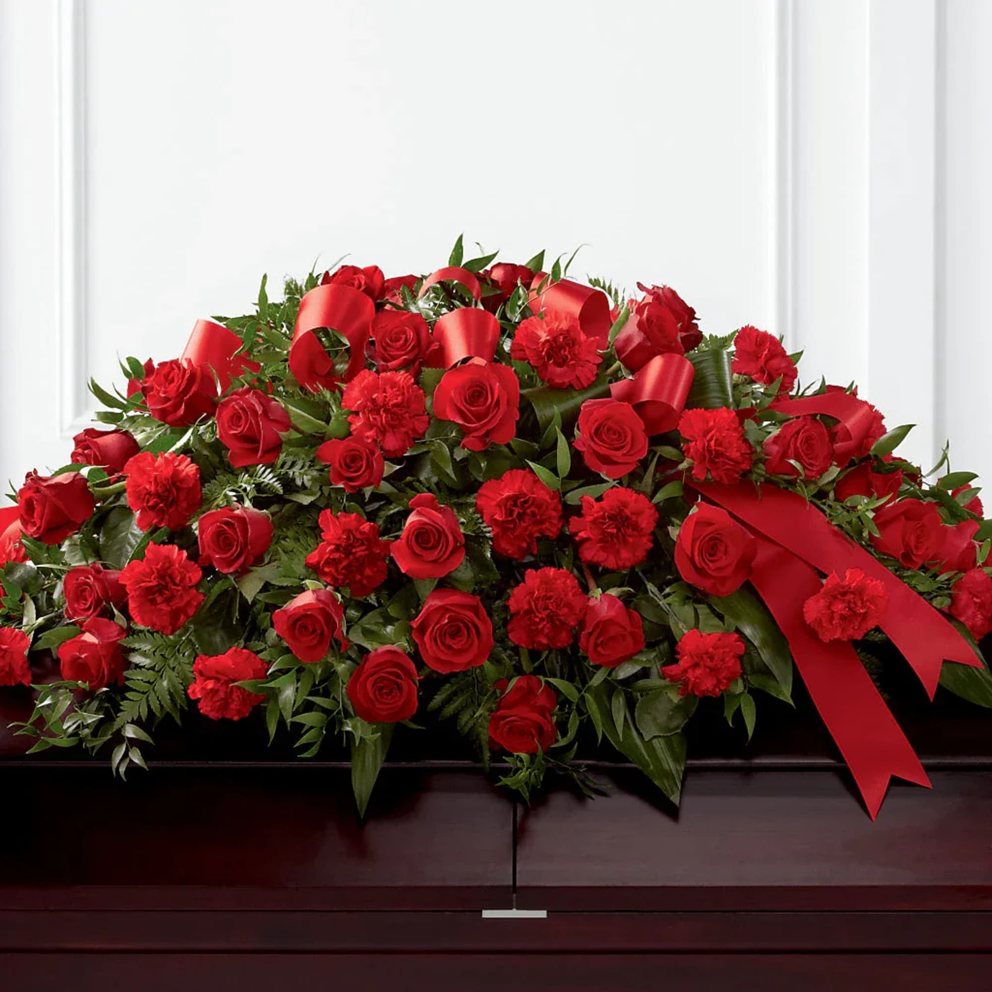 Red rose and carnation casket spray with red ribbons
