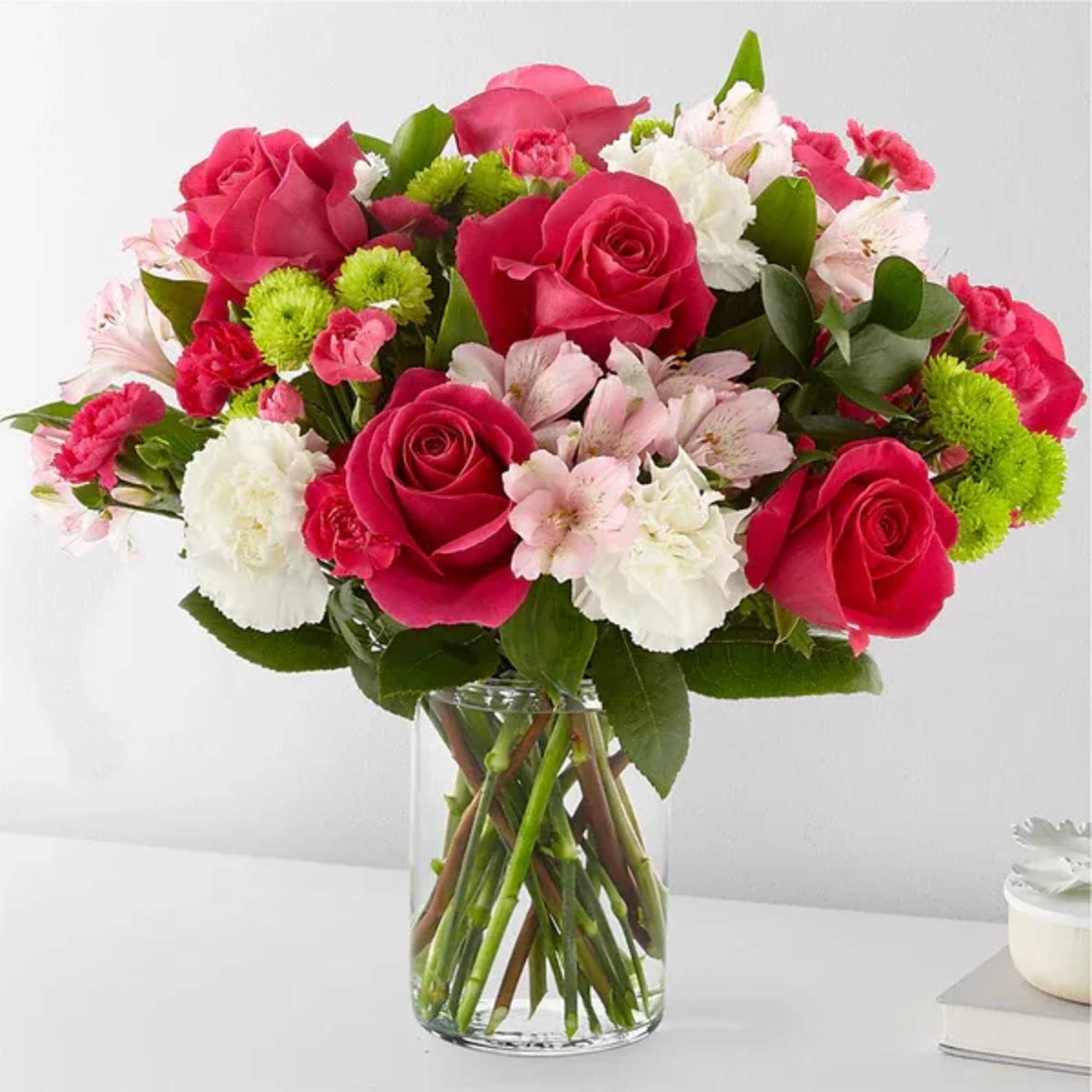 Bouquet of pink roses, white carnations, and green pompons in a glass vase