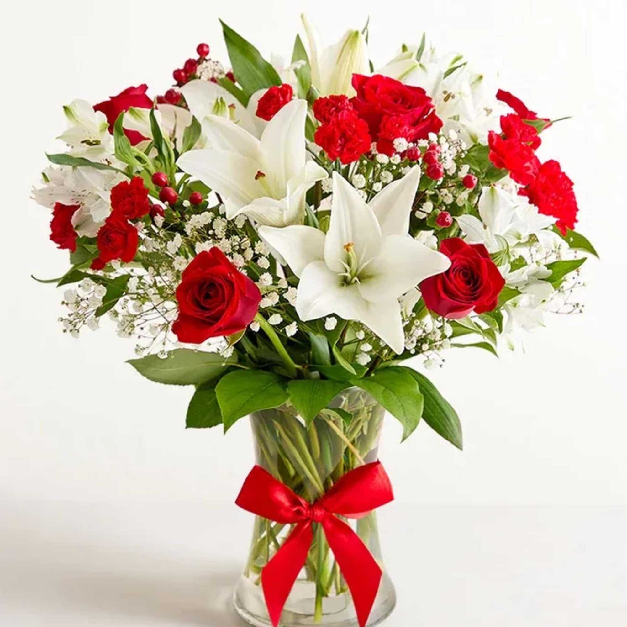 Red roses and white lilies in a clear glass vase with a red ribbon