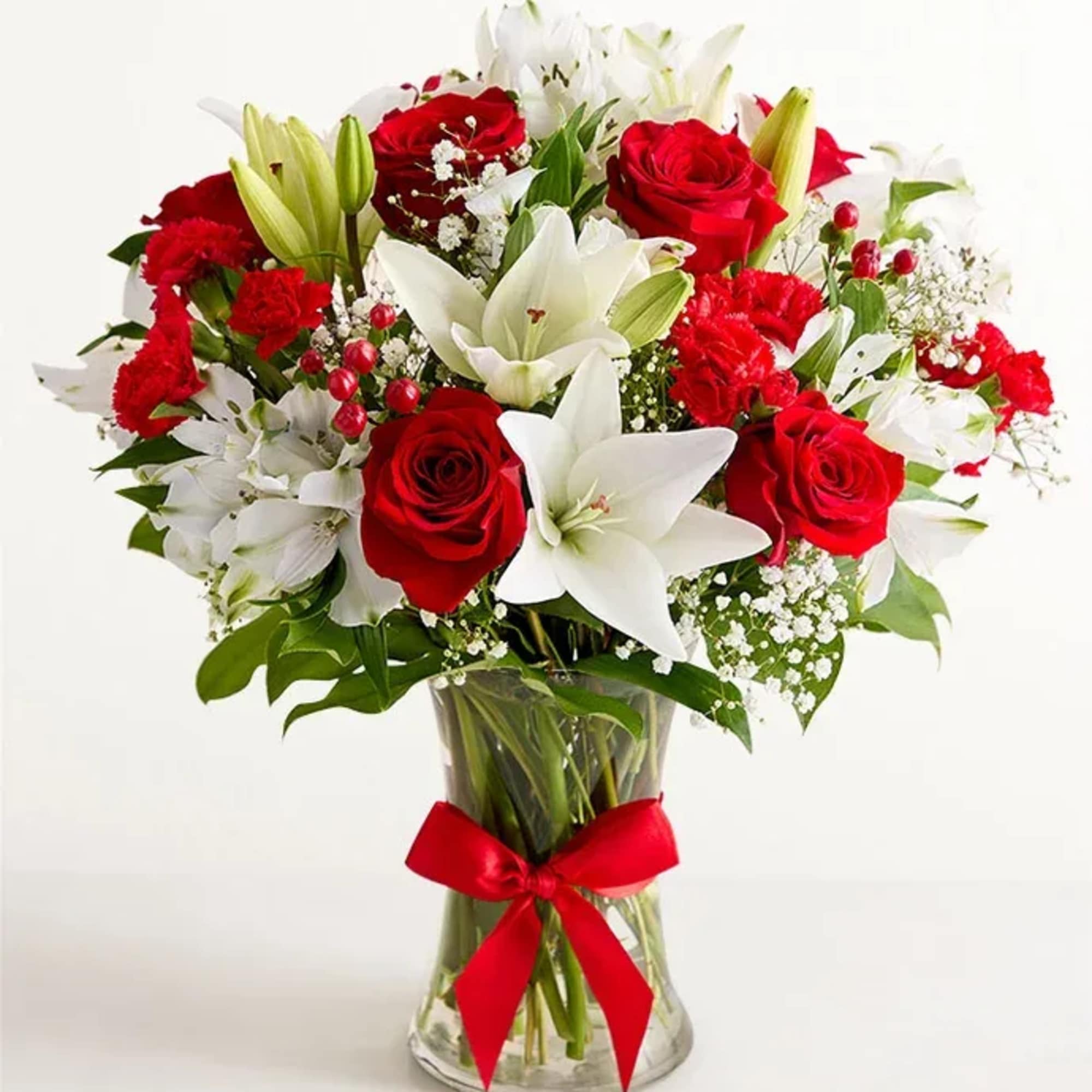 Red roses and white lilies in a clear glass vase with a red ribbon