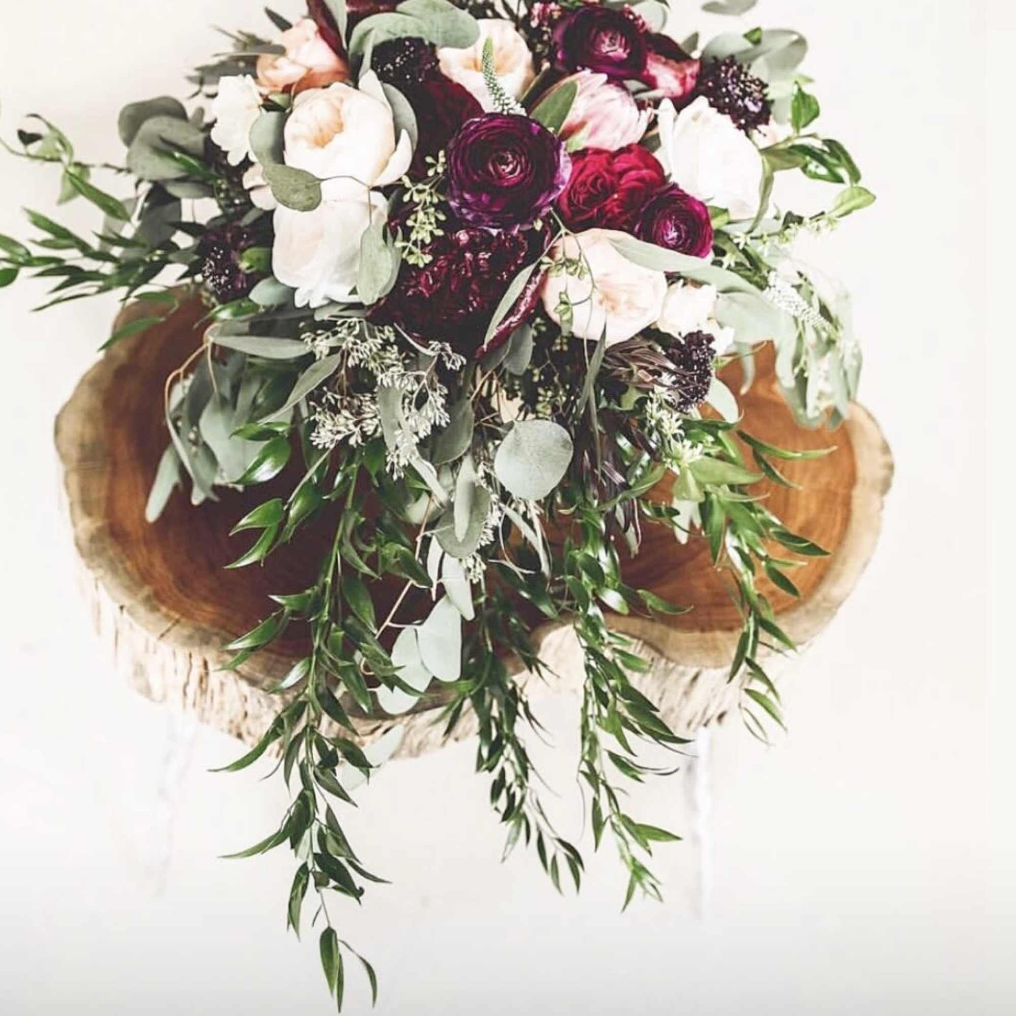 Bouquet of white and burgundy flowers with trailing greenery on a wood slice