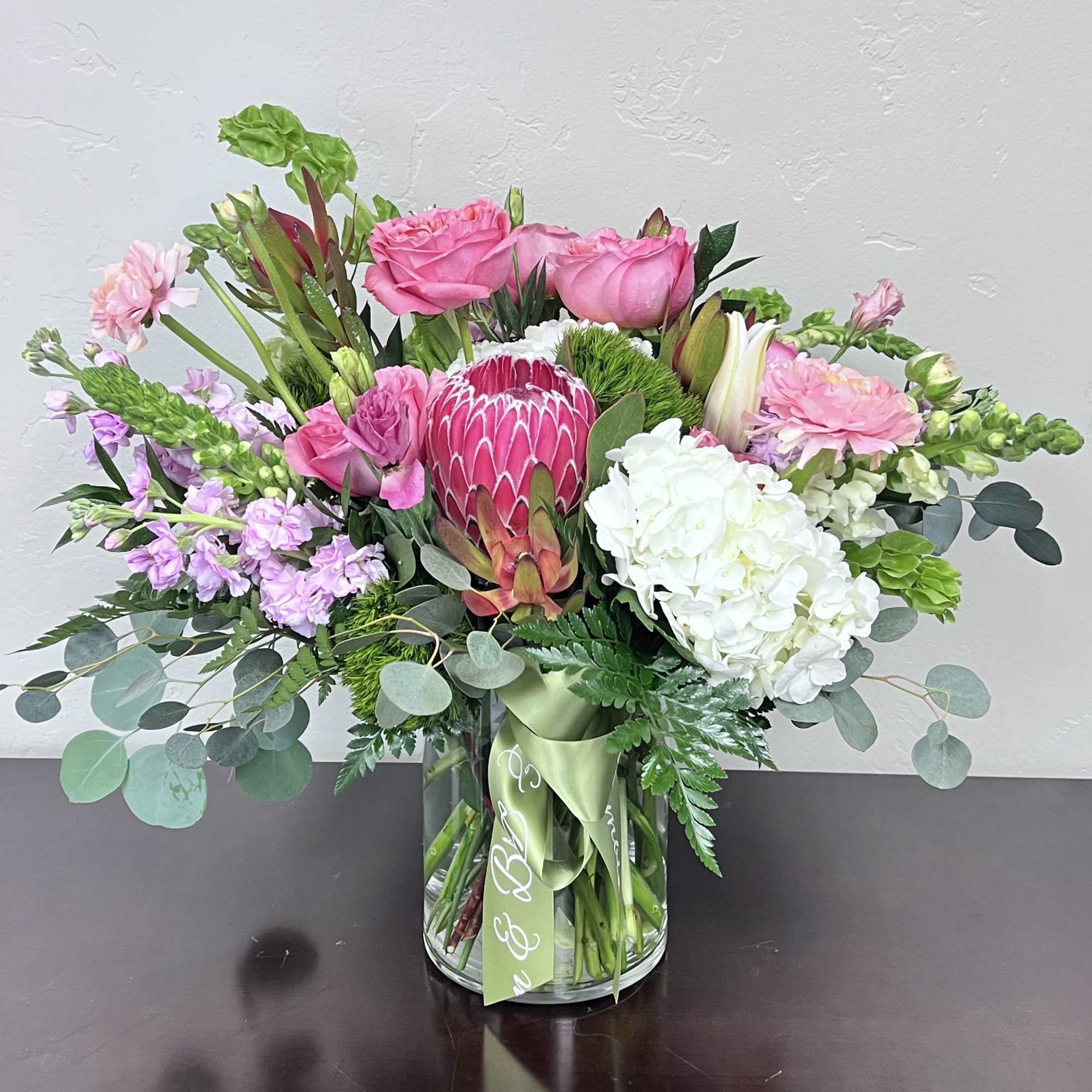 Pink and white mixed bouquet in a glass vase with a green ribbon