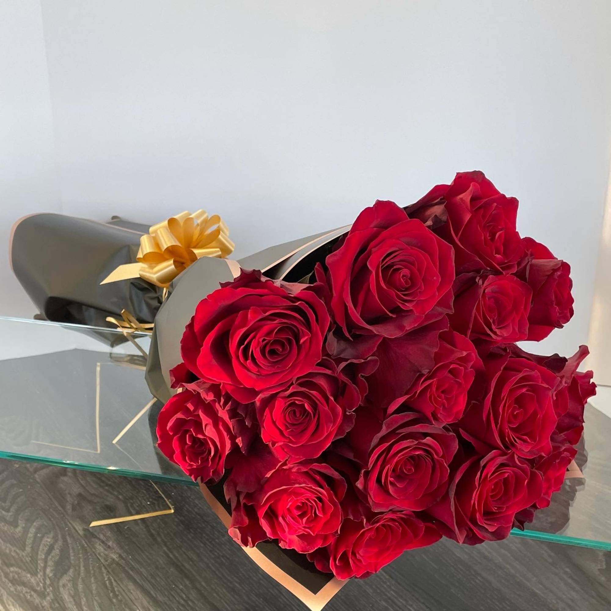 A compact hand-tied bouquet of deep red roses wrapped in matte black