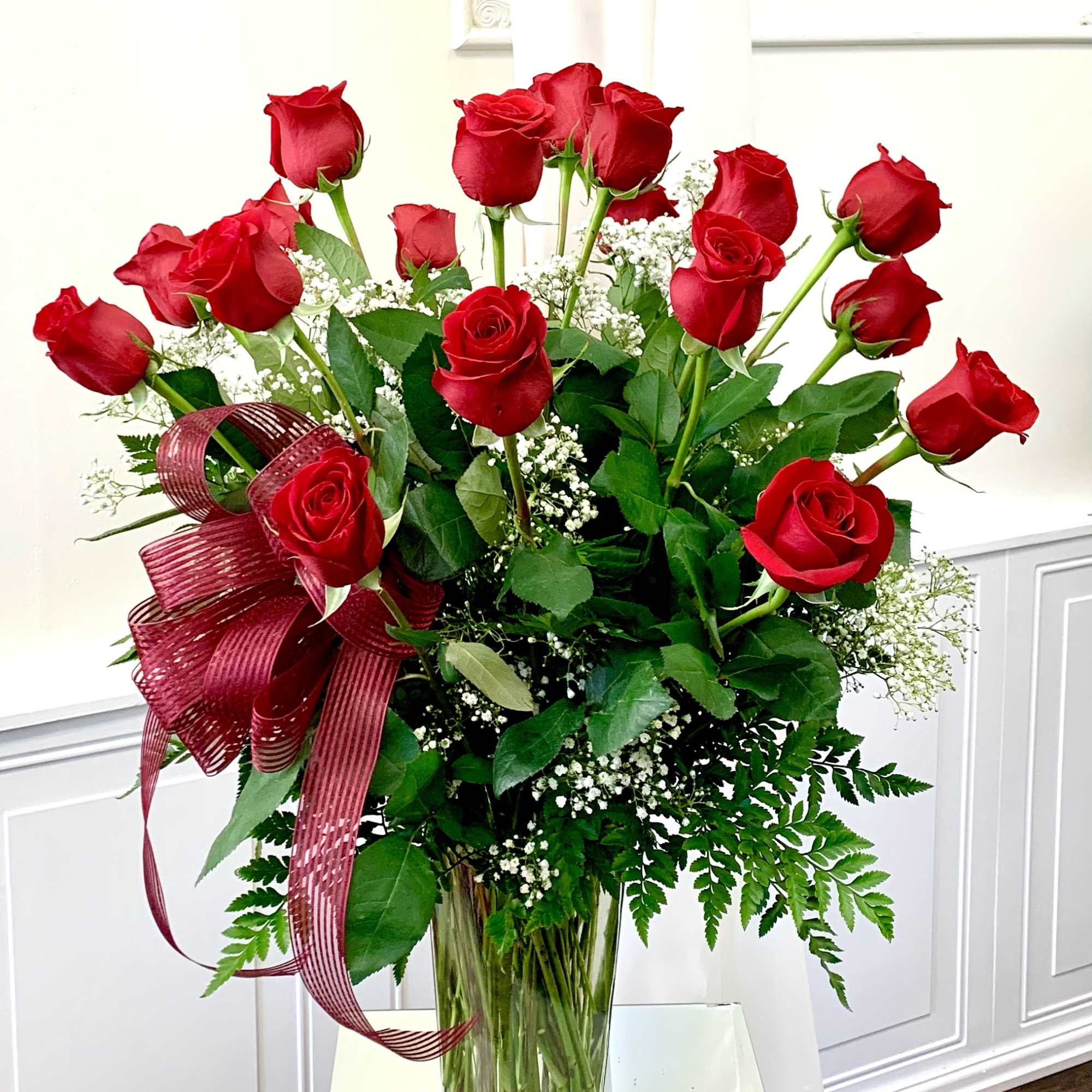 Red roses arranged in a clear glass vase with a burgundy ribbon