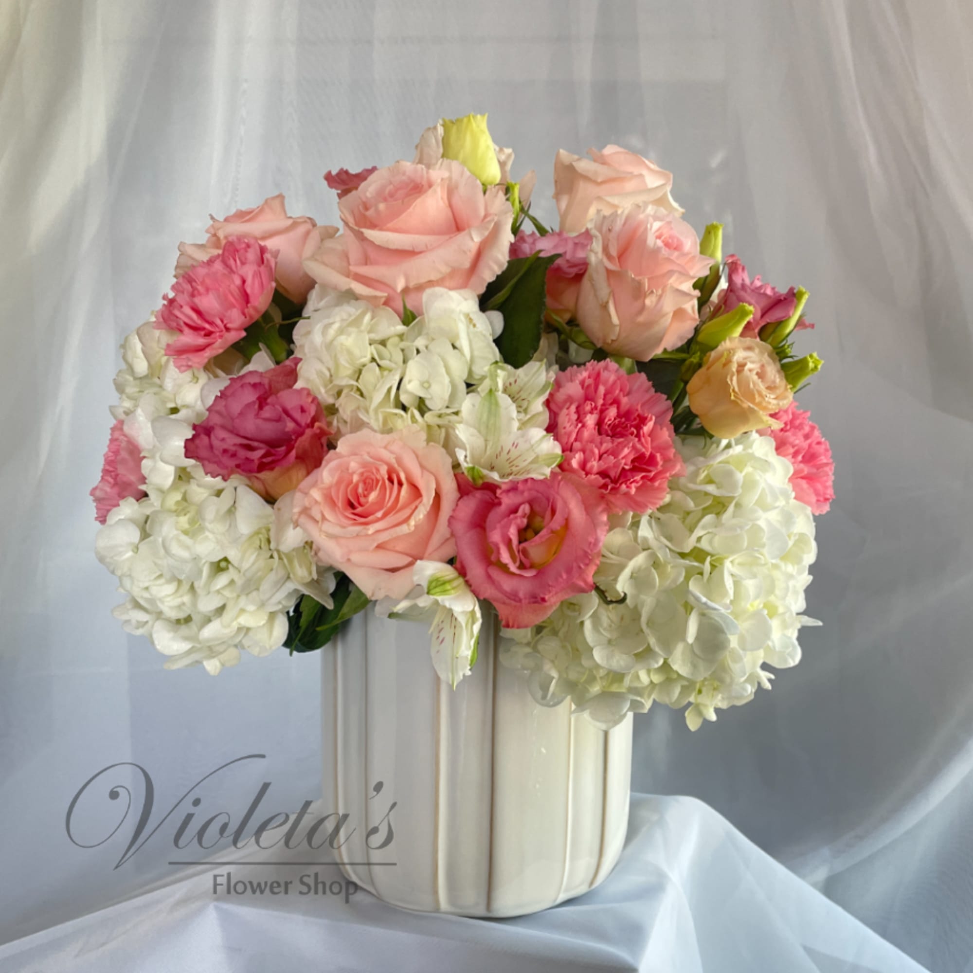 Pink roses and carnations arranged with white hydrangeas in a cream vase