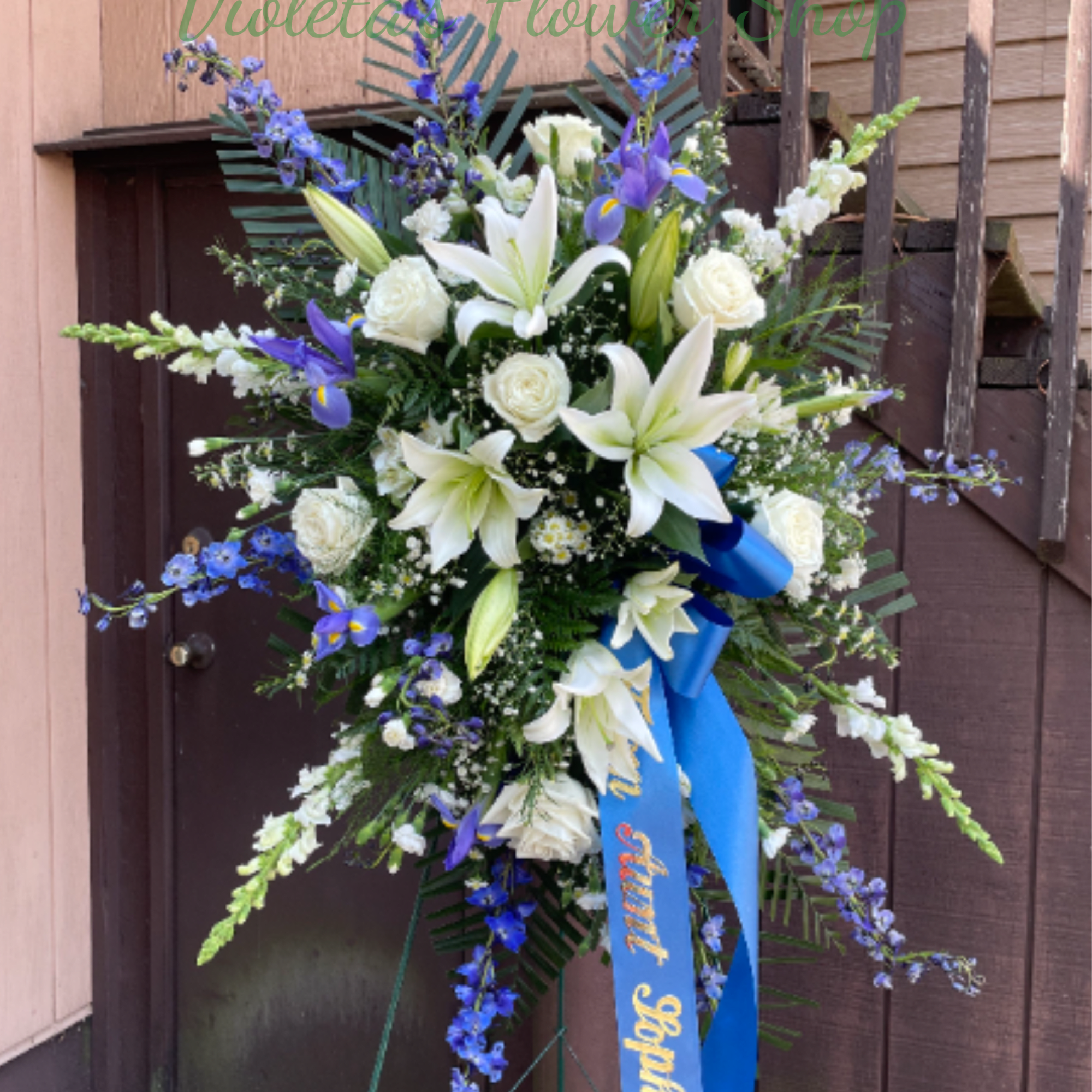 Standing floral spray with white lilies, white roses, and blue flowers