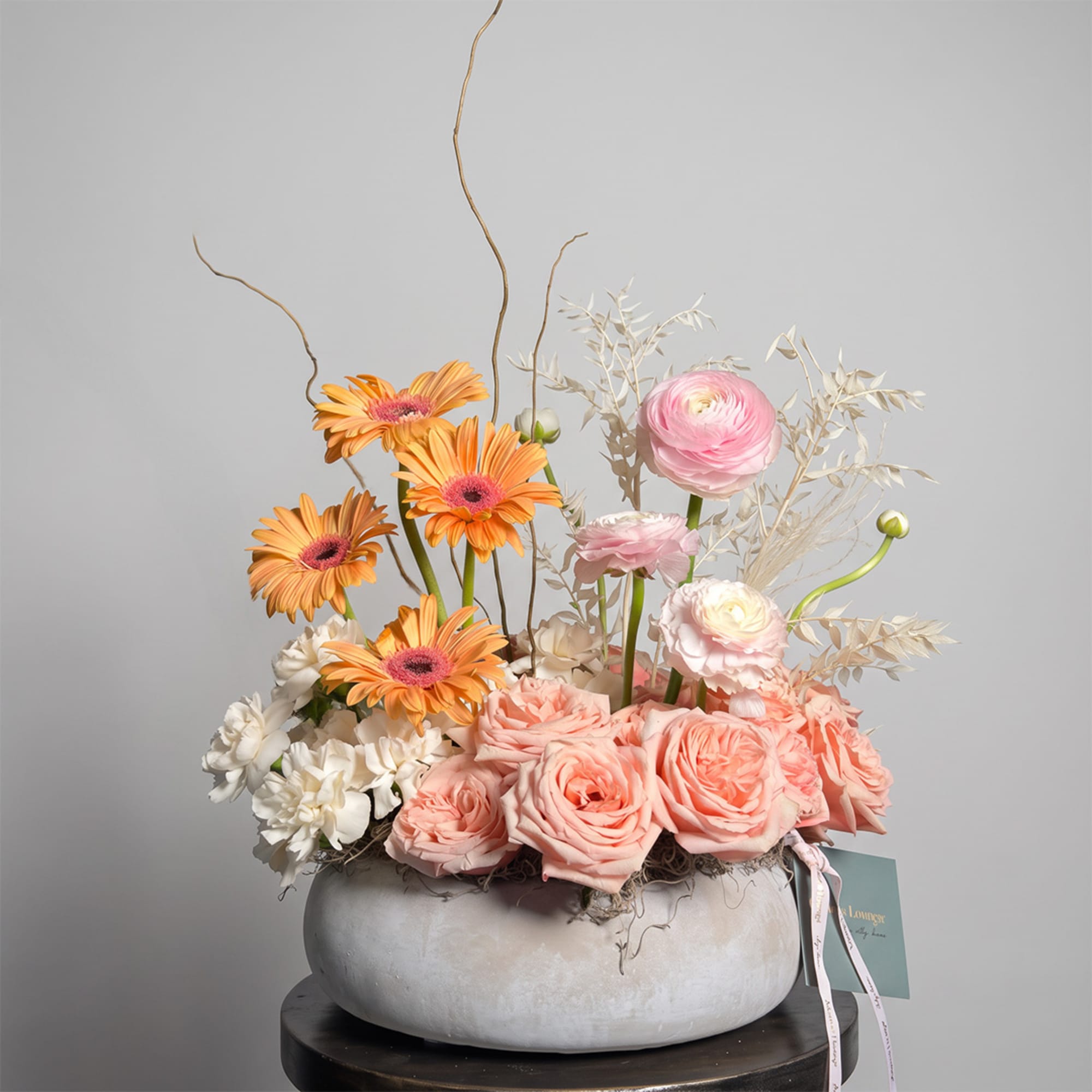 Pastel floral arrangement in a low gray bowl with pink roses and orange gerbera daisies