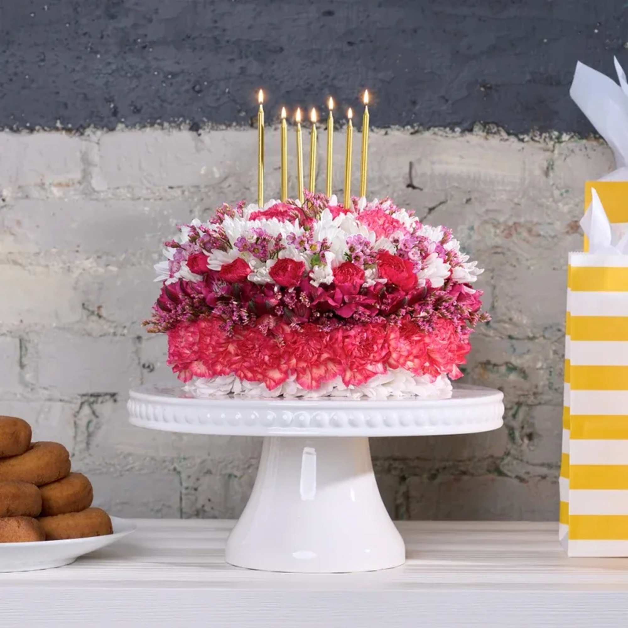Pink and white floral cake with lit gold candles on a white pedestal