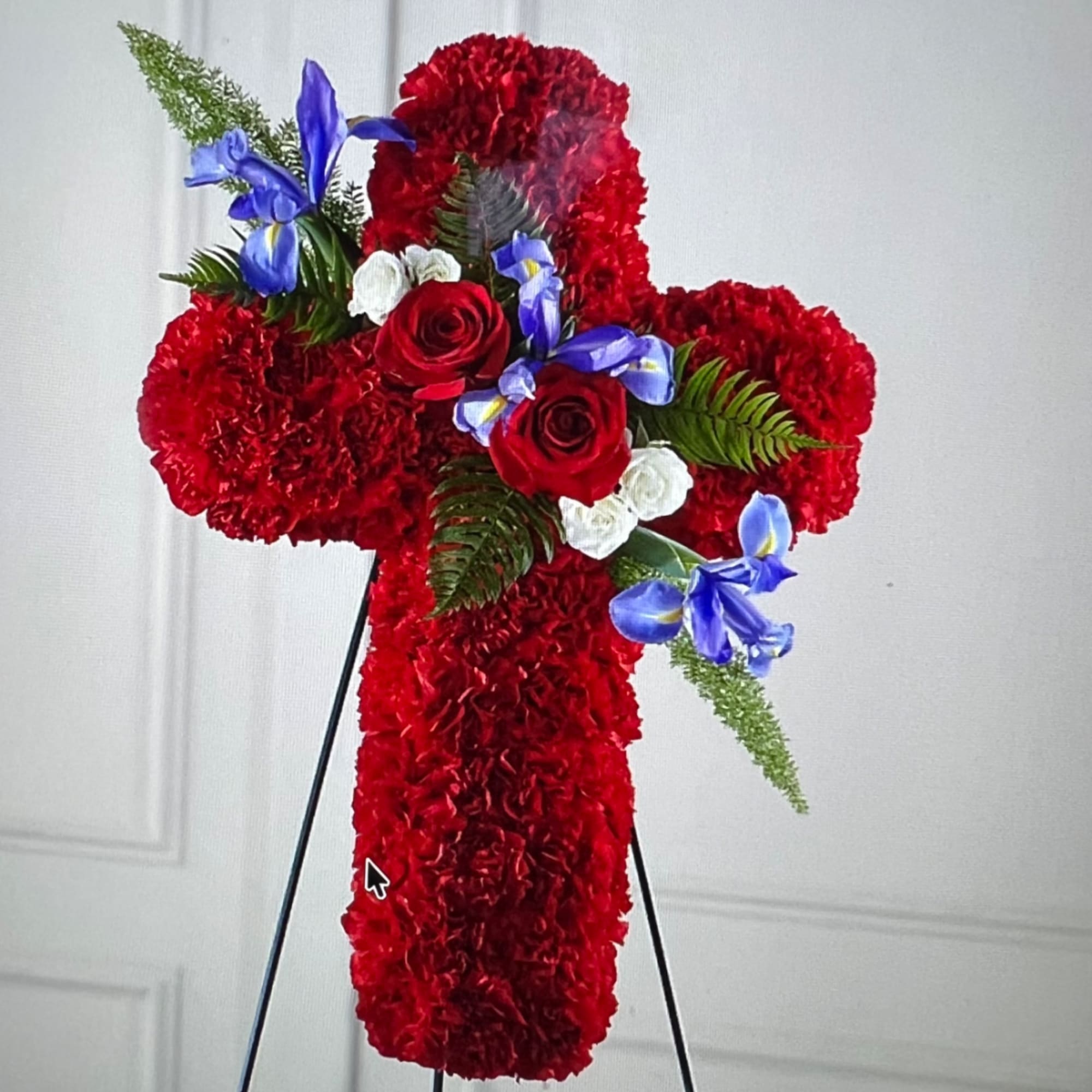 Red floral cross arrangement with roses and blue iris on a stand