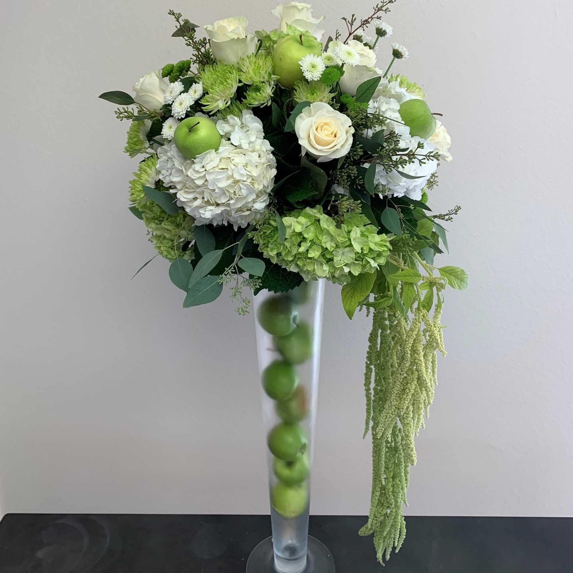 White and green floral arrangement in a tall glass vase with apples inside