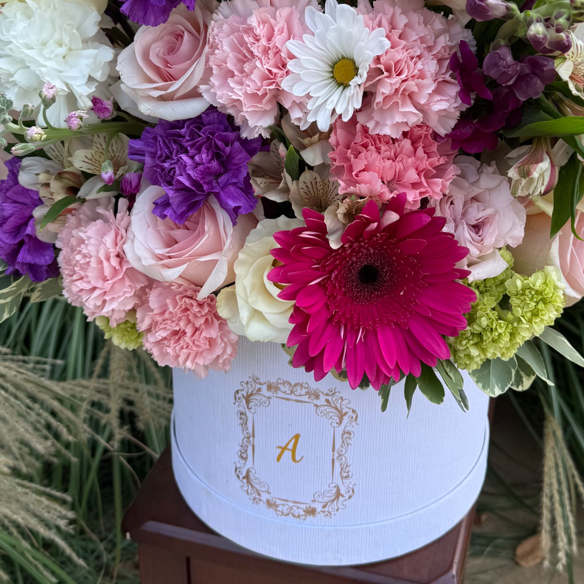 Mixed pink, purple, and white flowers arranged in a white hat box