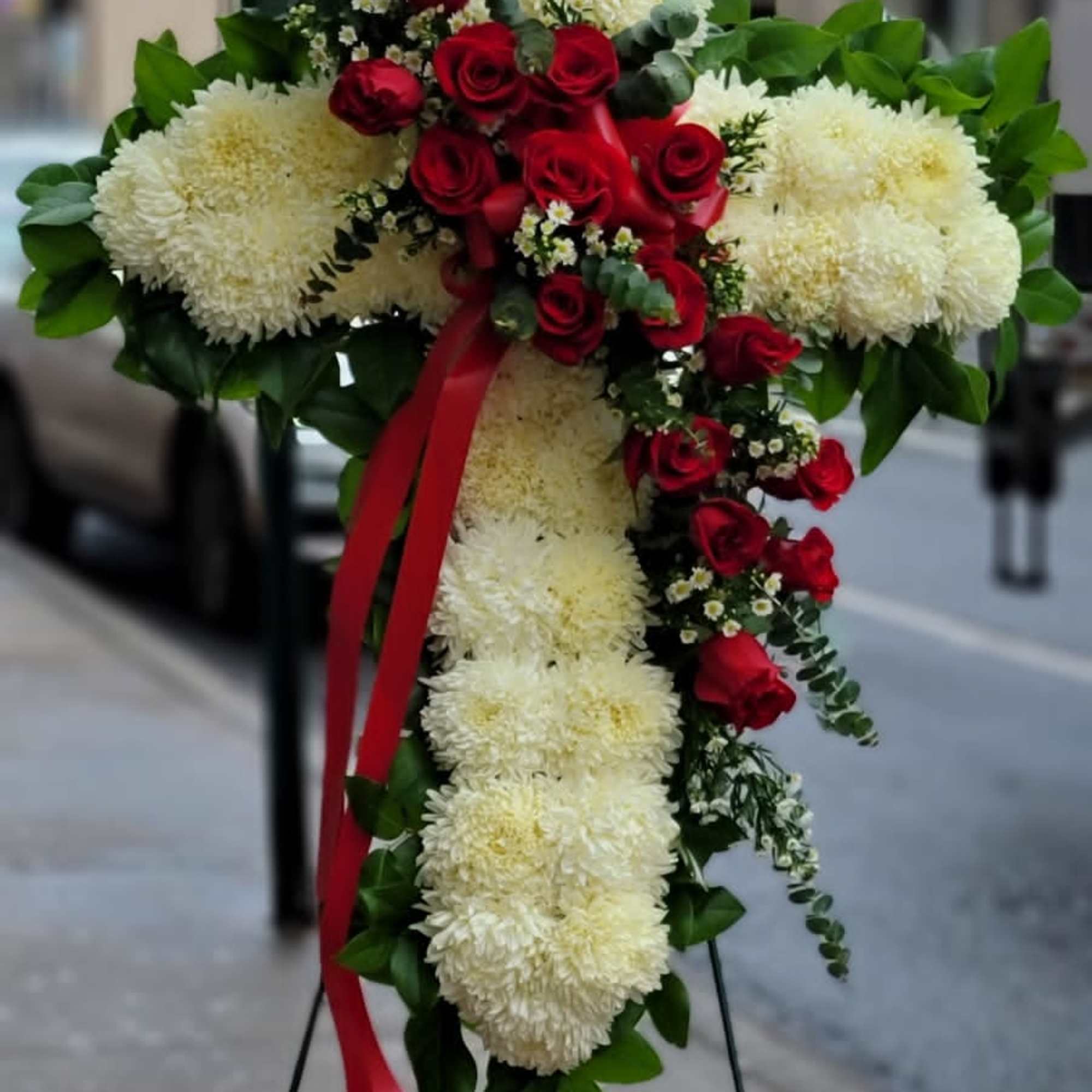 Cross-shaped floral spray with red roses and white chrysanthemums on a stand