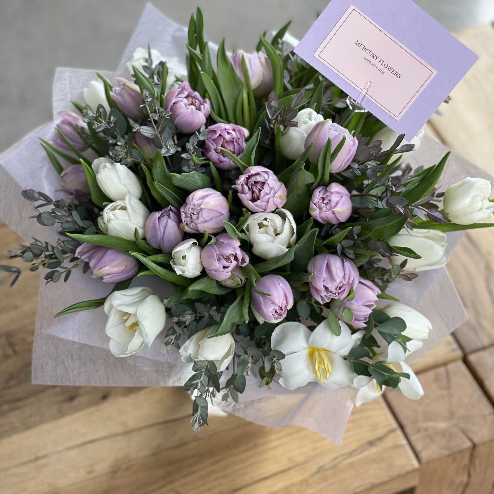 Bouquet of pink and white tulips with greenery and a purple card