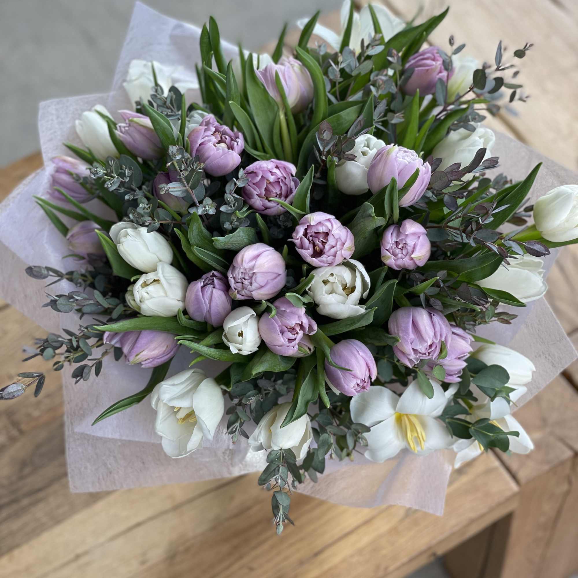 Bouquet of pink and white tulips with greenery wrapped in pale paper