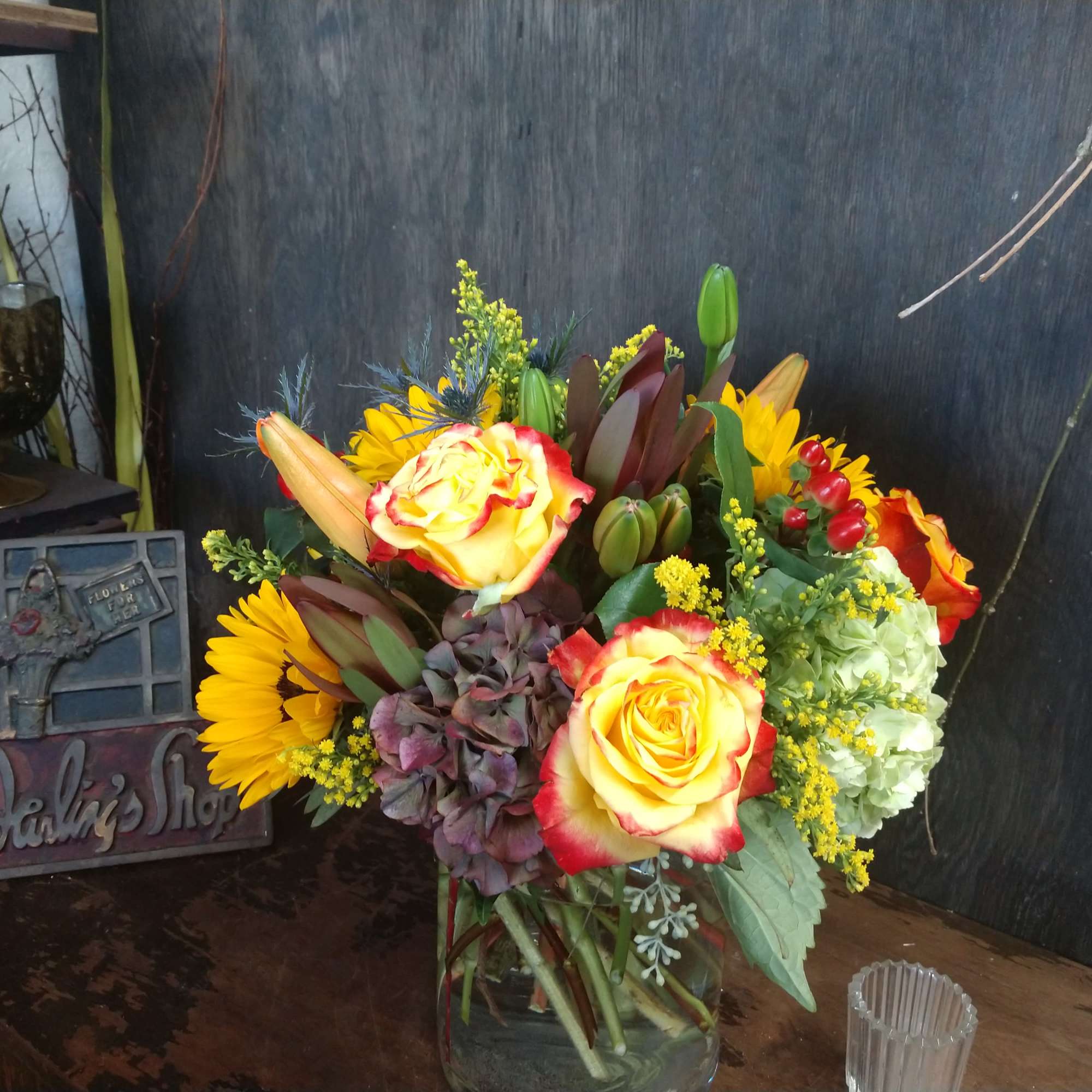 Mixed bouquet of yellow roses, sunflowers, lilies, and hydrangea in a glass vase