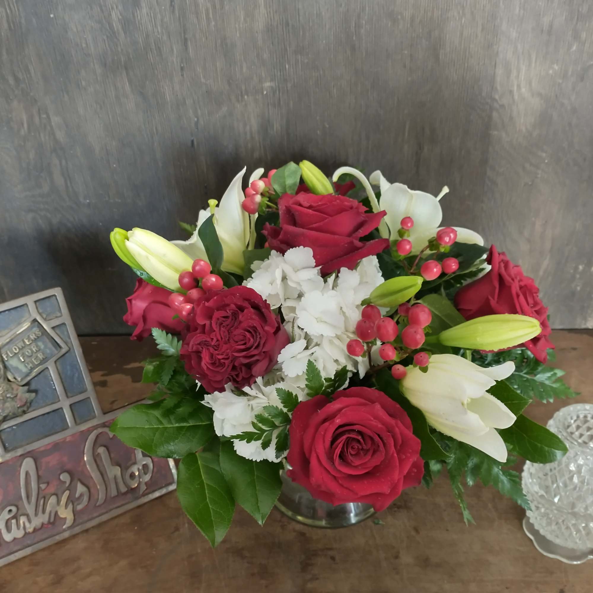 Red roses and white lilies arranged in a low vase with berry accents