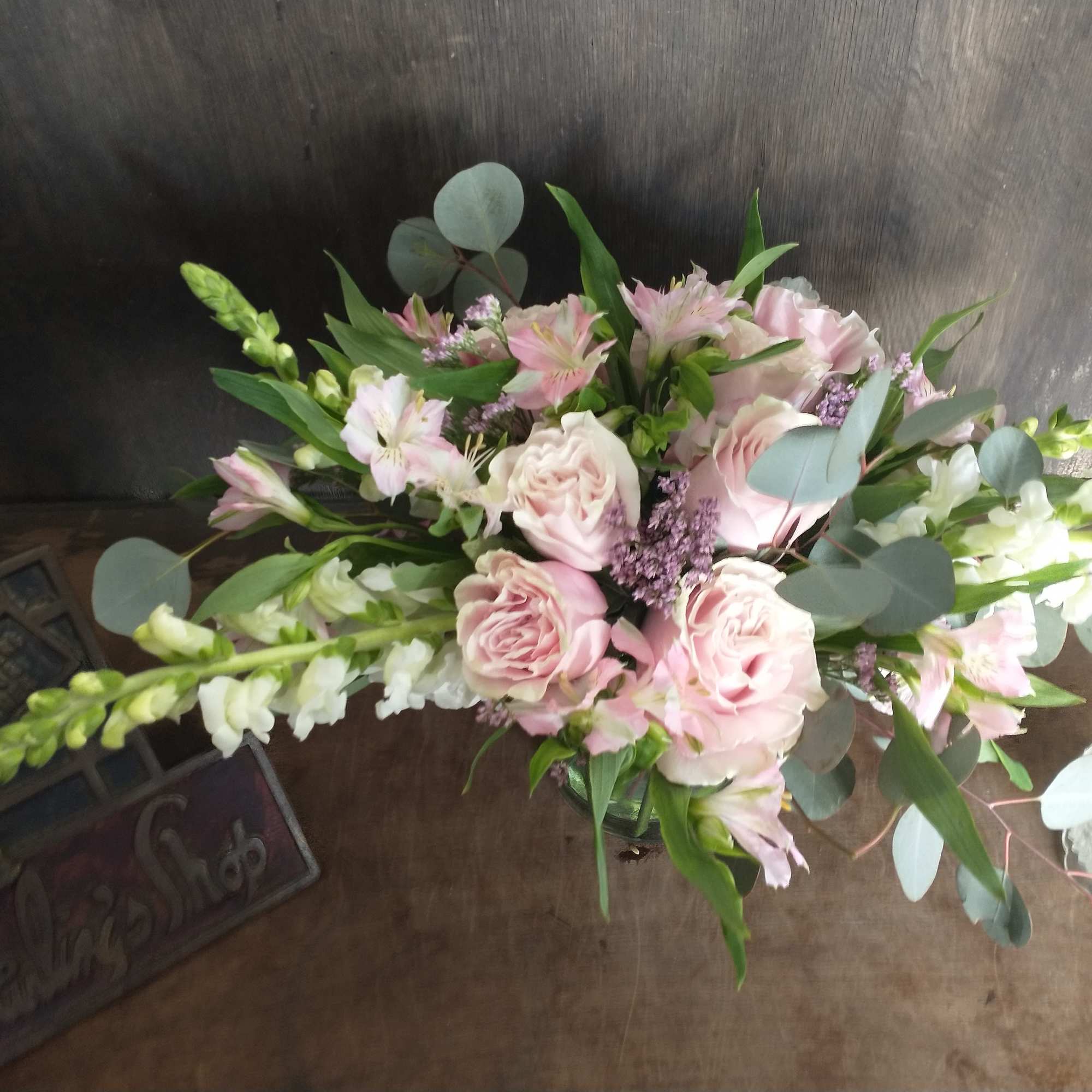 Pastel arrangement of pink roses, alstroemeria, and white snapdragons in a vase on a wooden table