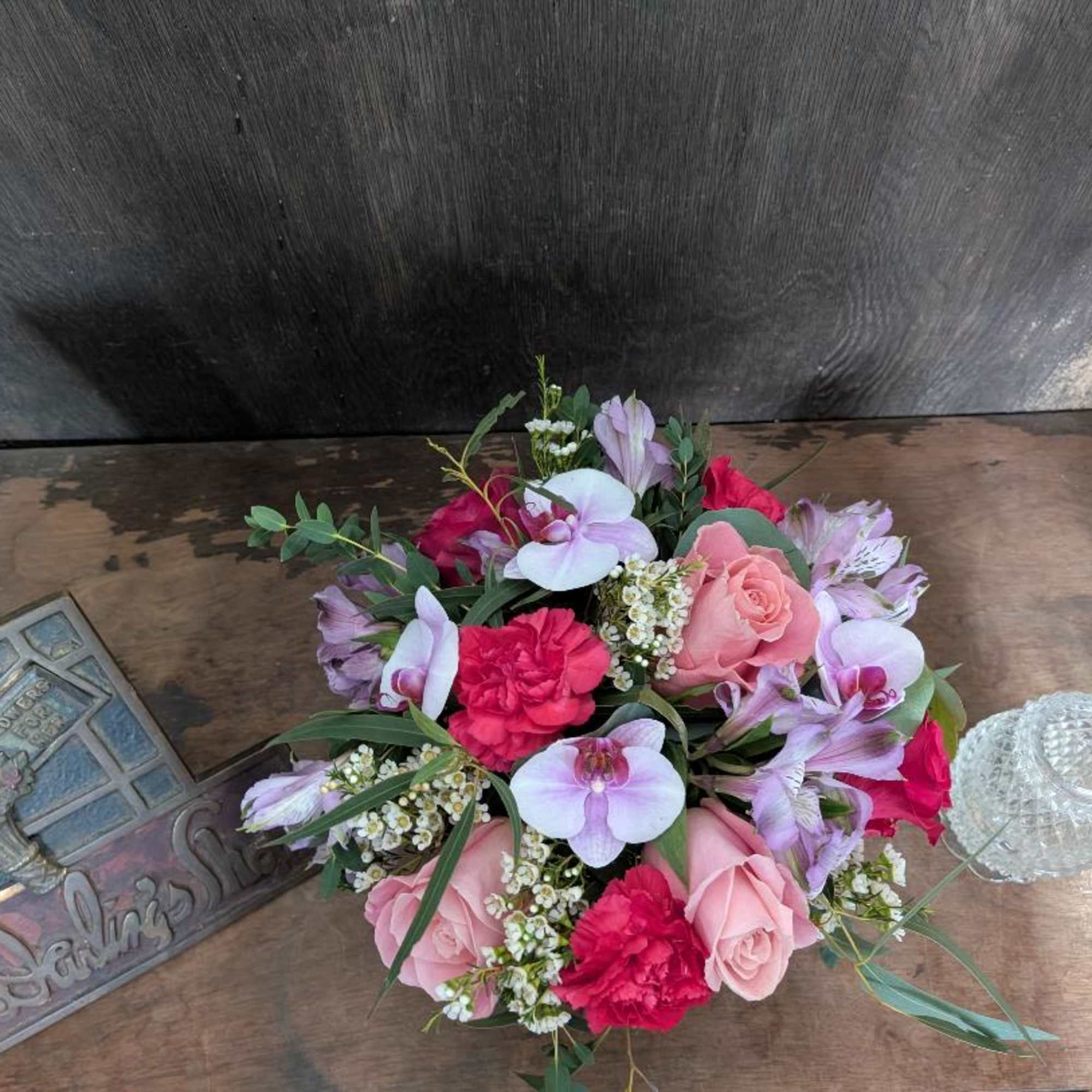 Pink and lavender bouquet with roses, orchids, and carnations on a wooden table