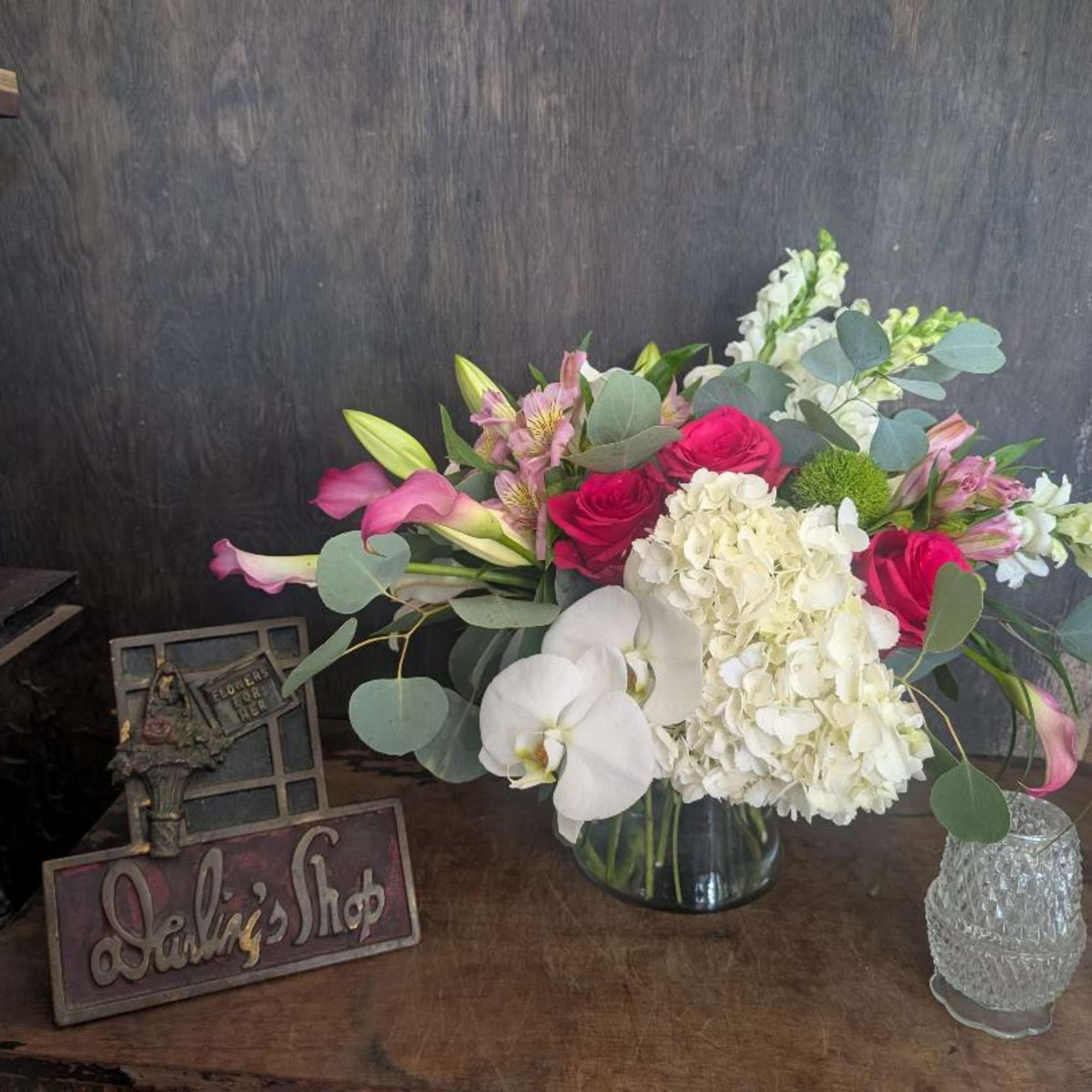 Mixed bouquet with pink roses, white hydrangea, orchids, and calla lilies in a glass vase