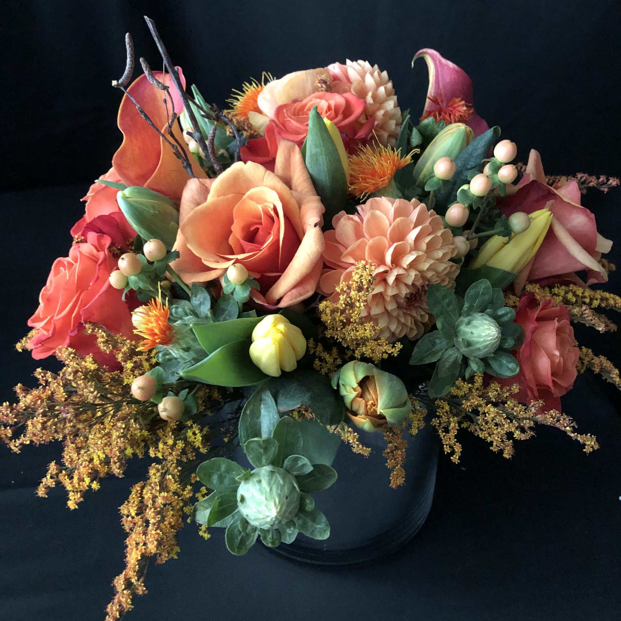 Mixed bouquet of coral and peach flowers in a dark container