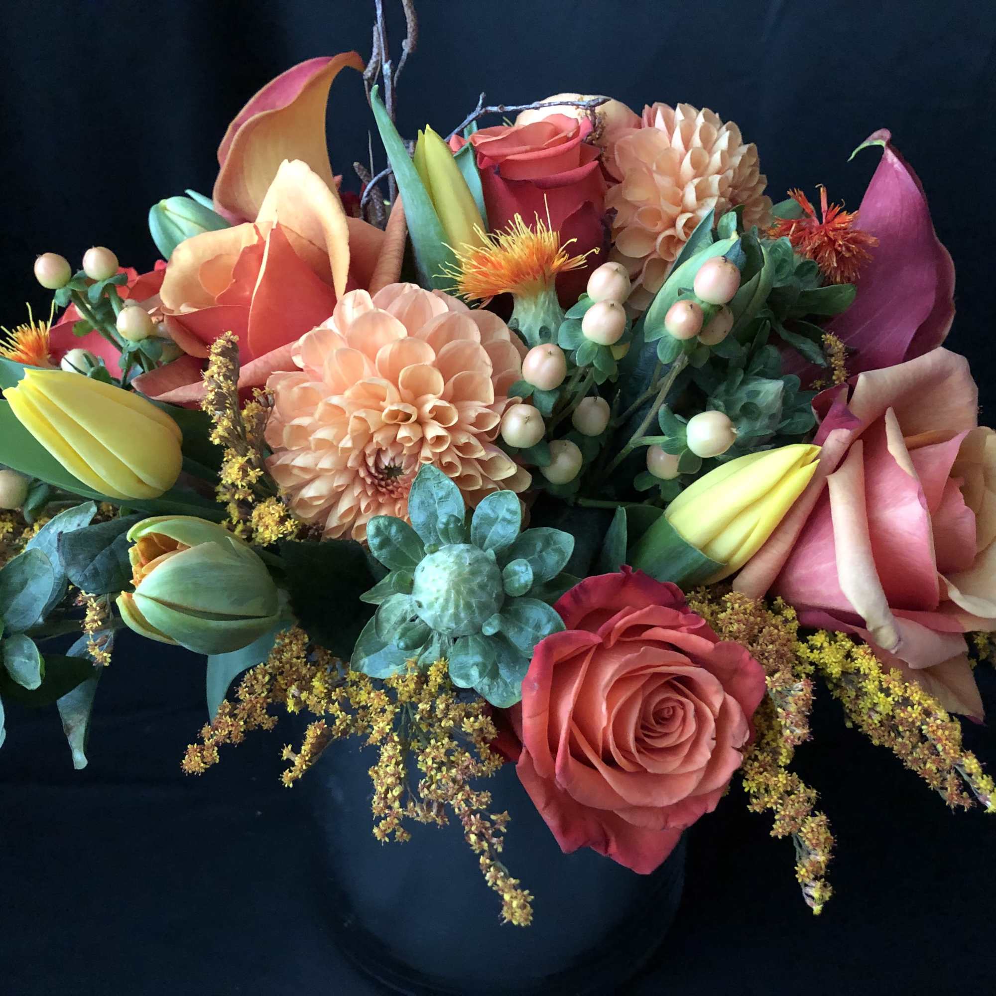 Colorful bouquet with roses, calla lilies, and dahlias in a dark vase