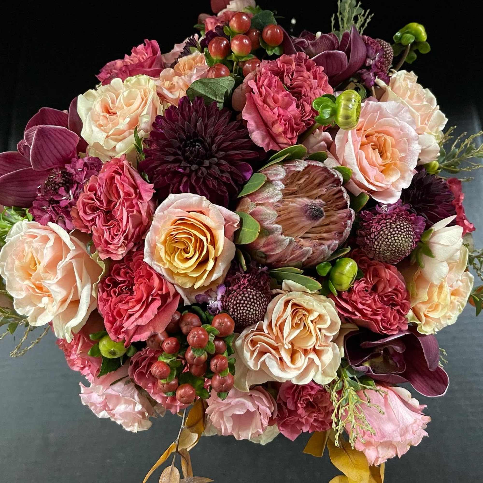 Large bouquet of pink, peach, and burgundy flowers with protea and roses
