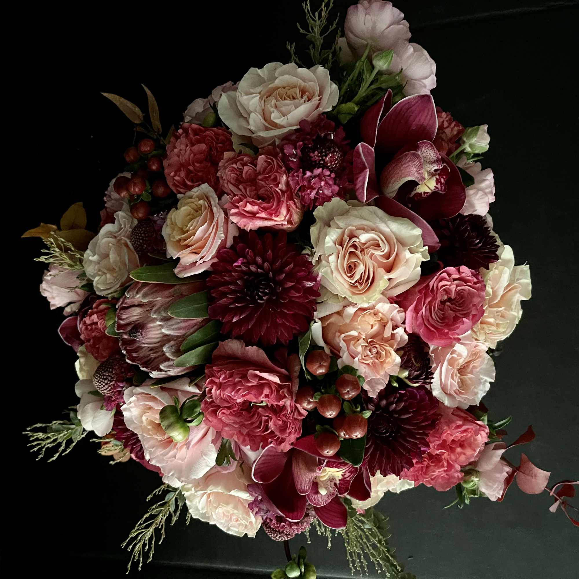 Round bouquet of pink, cream, and burgundy flowers on a dark background