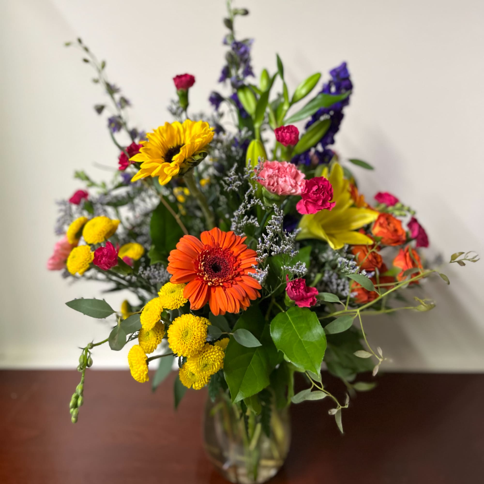 Mixed bouquet with sunflowers, lilies, carnations, and gerbera daisies in a glass vase