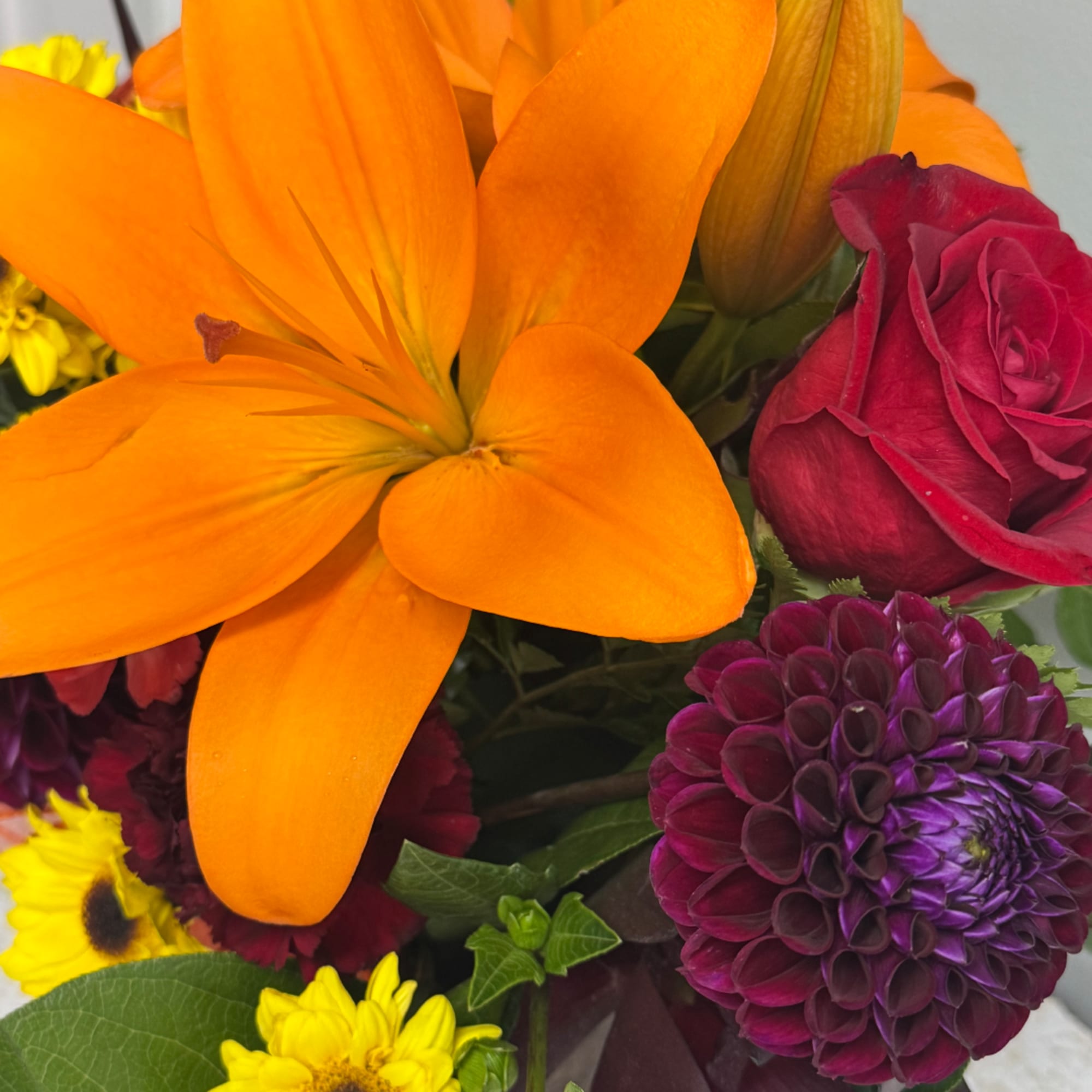 Close-up bouquet with orange lilies, a red rose, and purple blooms