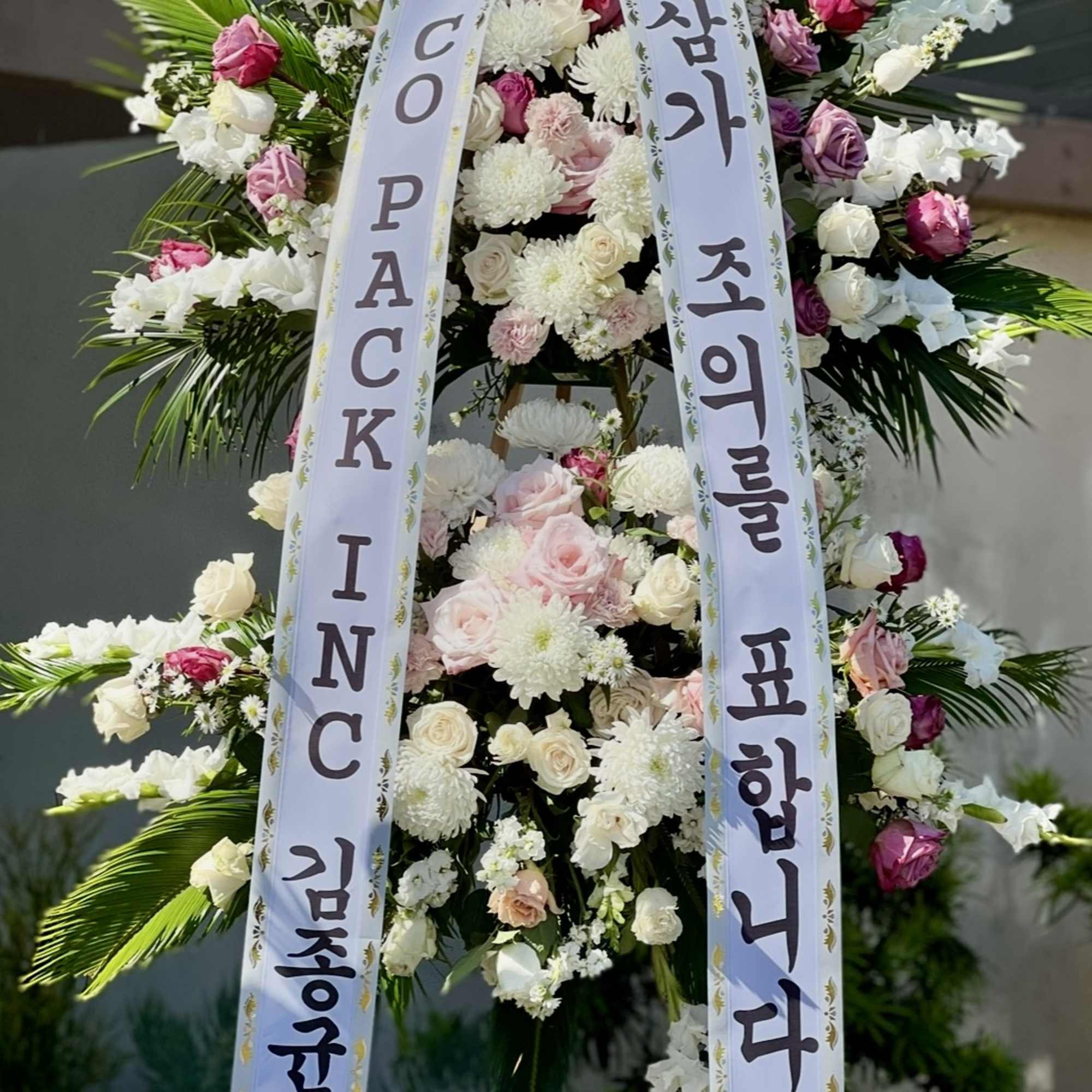 Standing floral wreath with pink and white flowers and two condolence ribbons