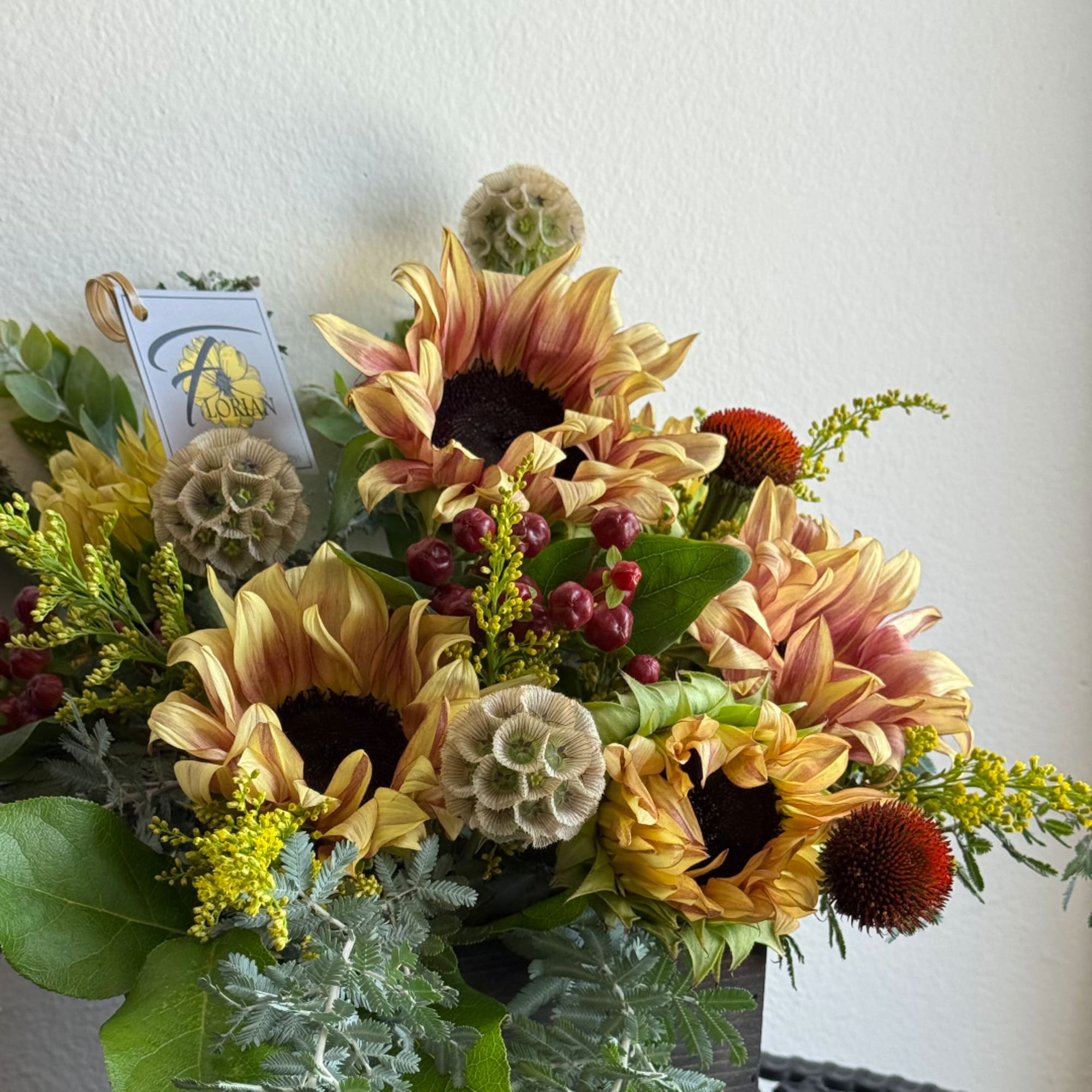 Sunflower arrangement with berries and seed pods in a dark container