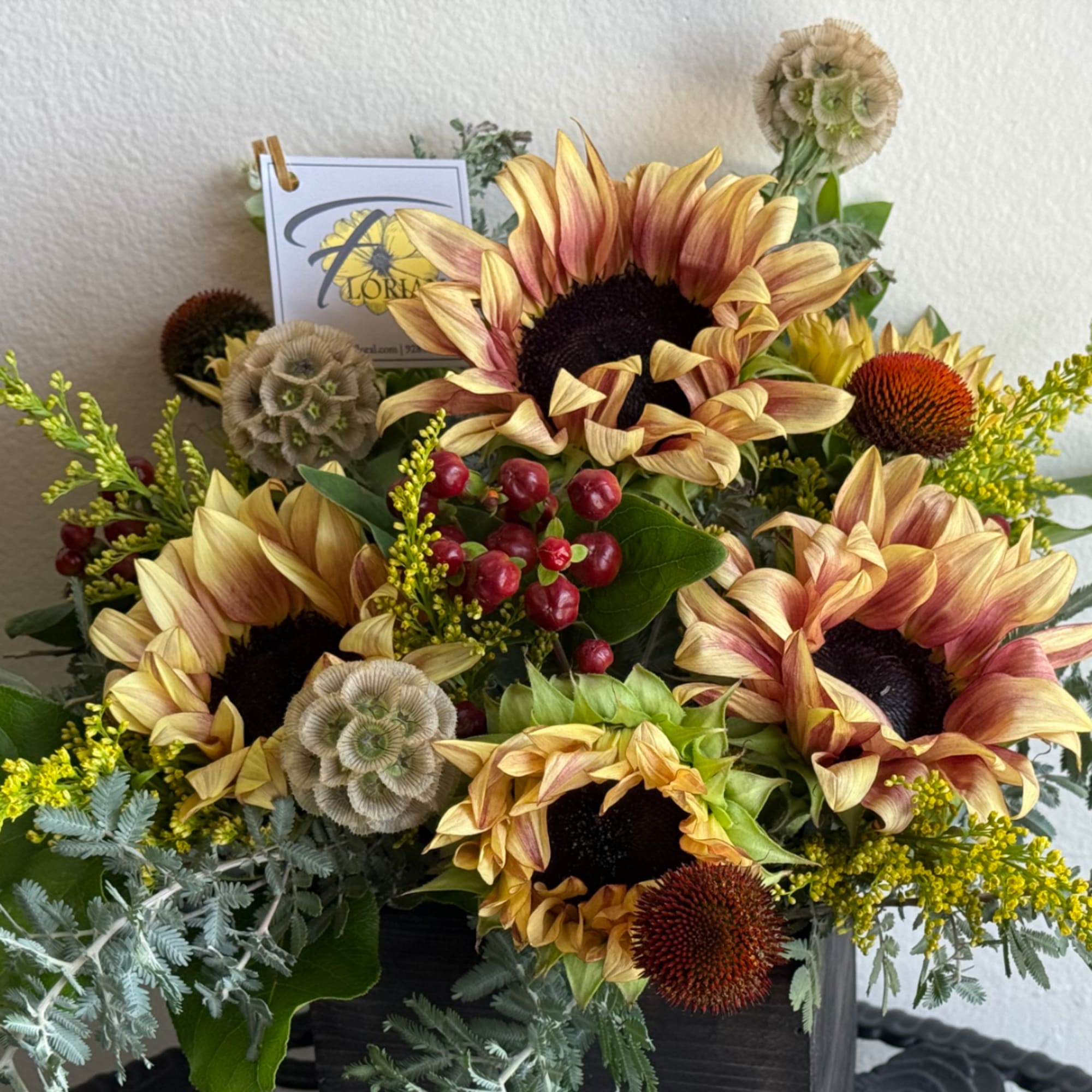 Sunflower arrangement with red berries in a dark container