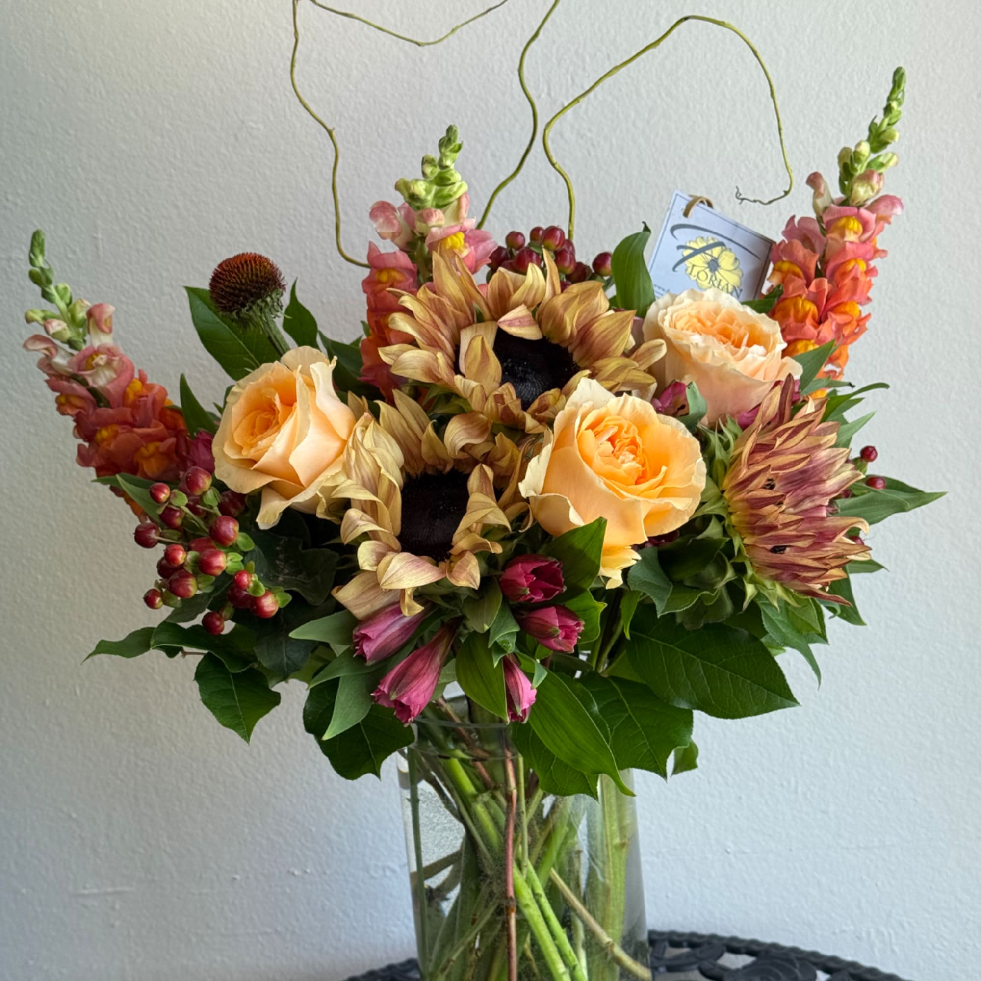 Bouquet of sunflowers, peach roses, and snapdragons in a glass vase