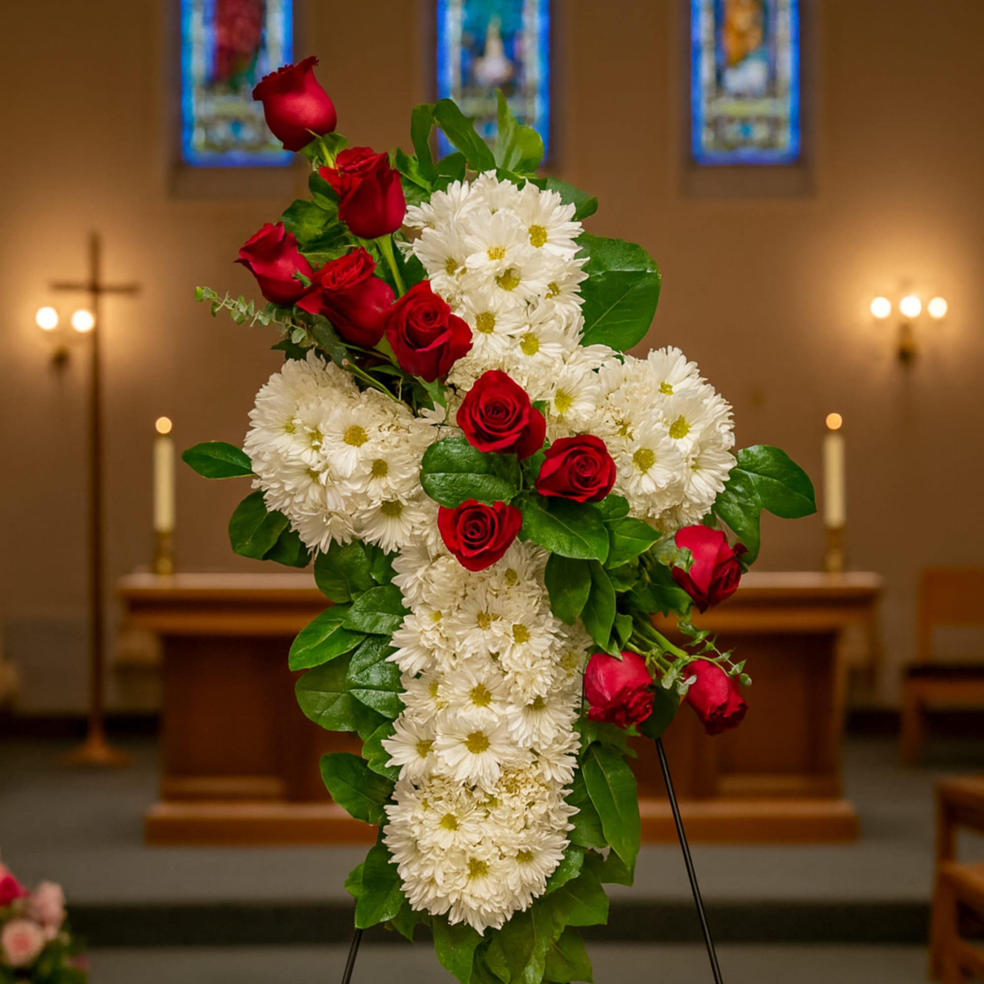 Standing floral spray with red roses and white daisies on an easel
