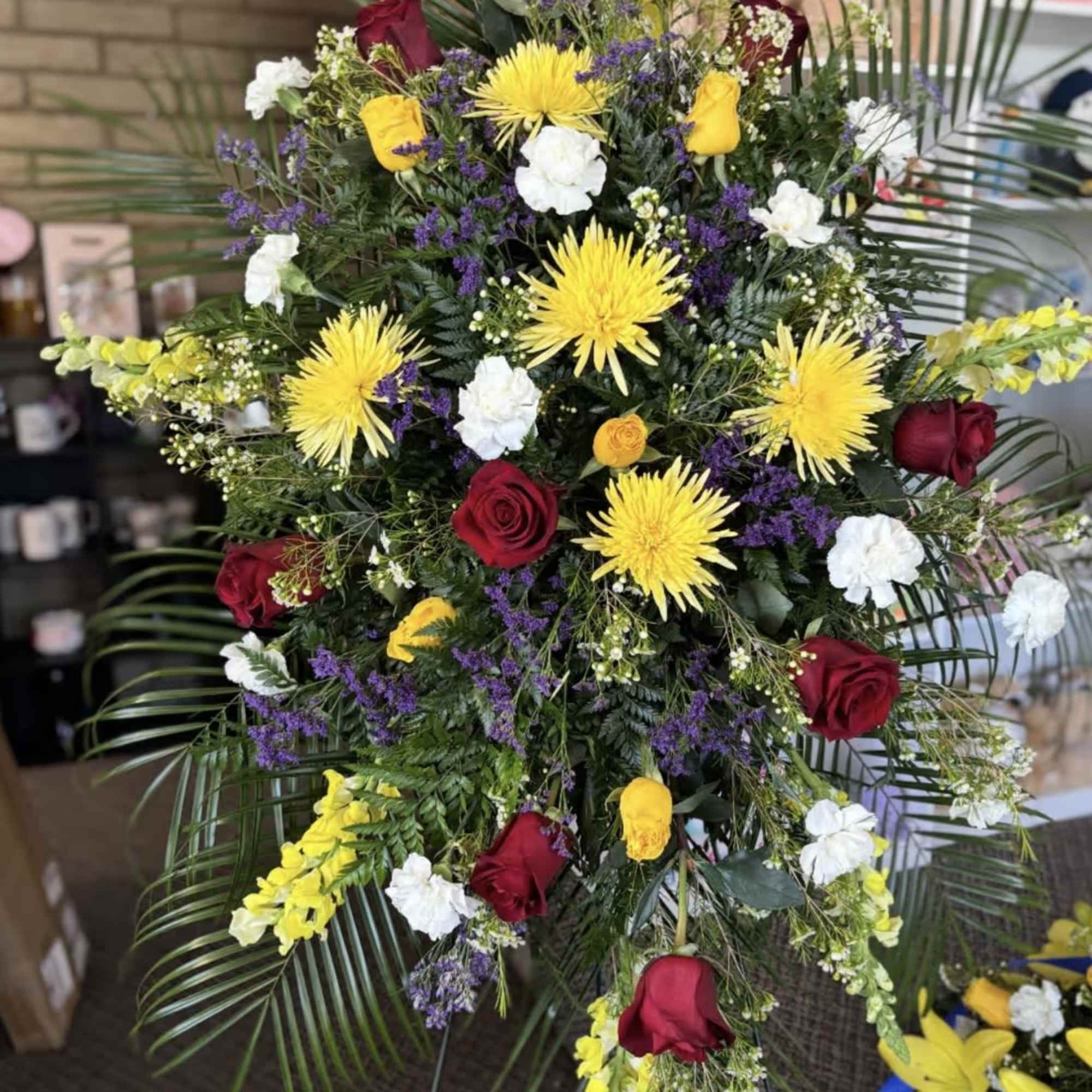 Large standing floral spray with red roses, yellow blooms, and white accents
