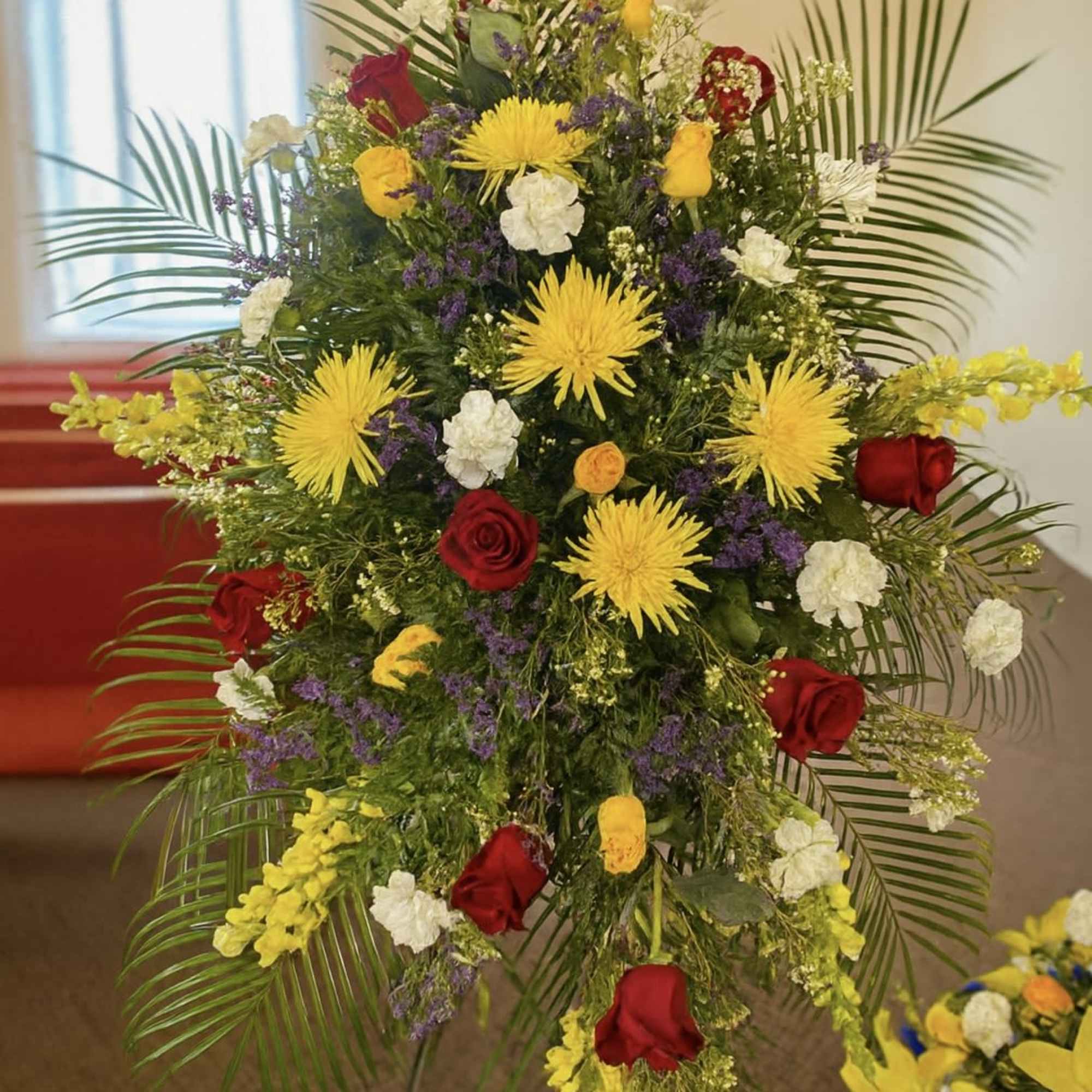 Tall funeral spray with red roses, yellow spider mums, and white carnations