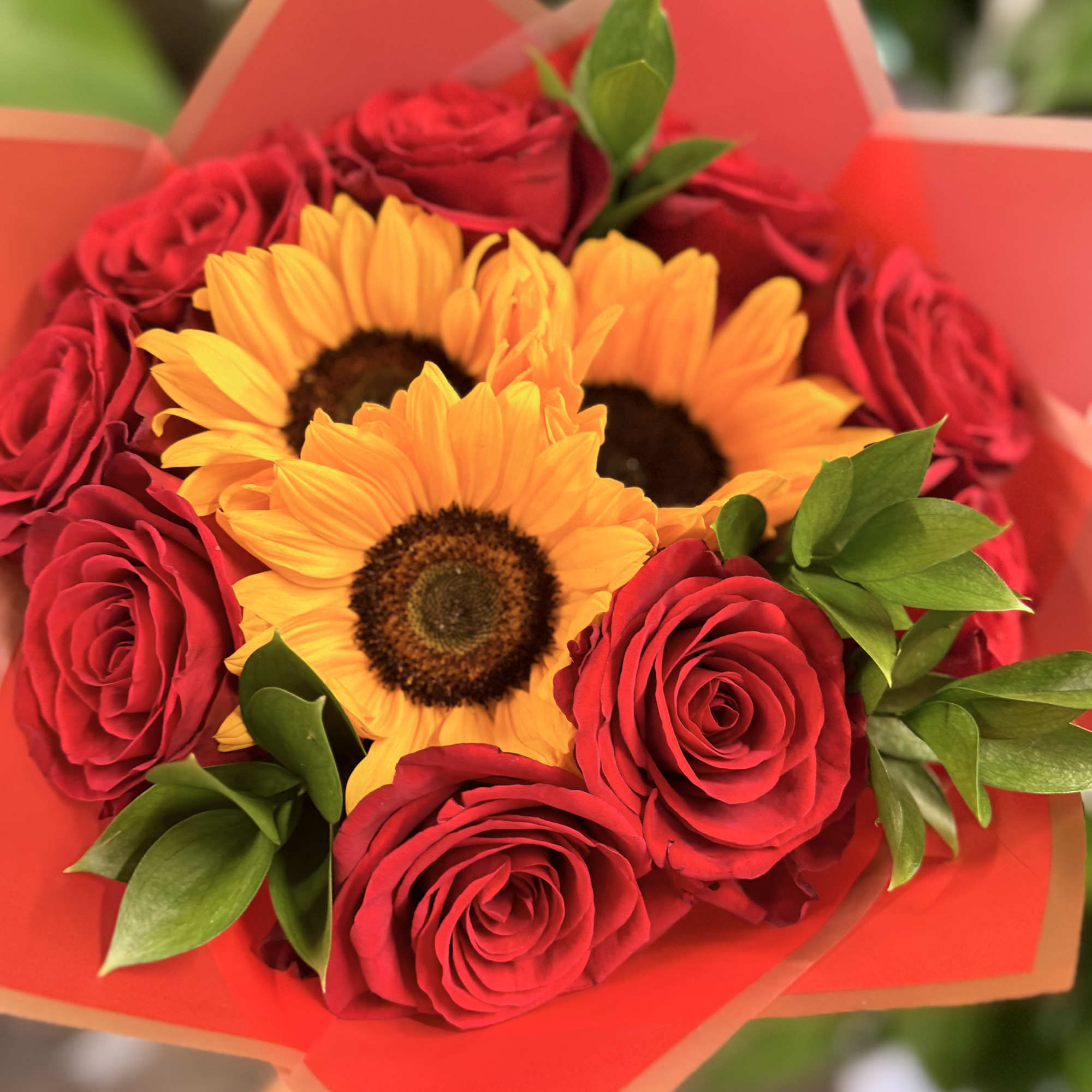 Bouquet of red roses and yellow sunflowers wrapped in orange paper