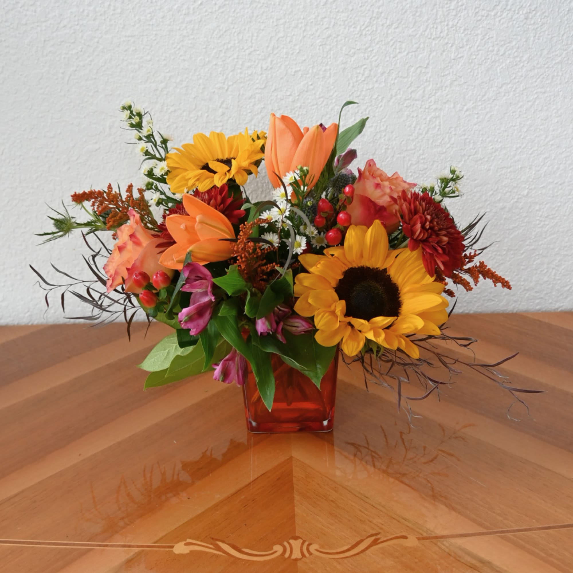 Mixed bouquet in a red glass vase with sunflowers, lilies, and orange blooms