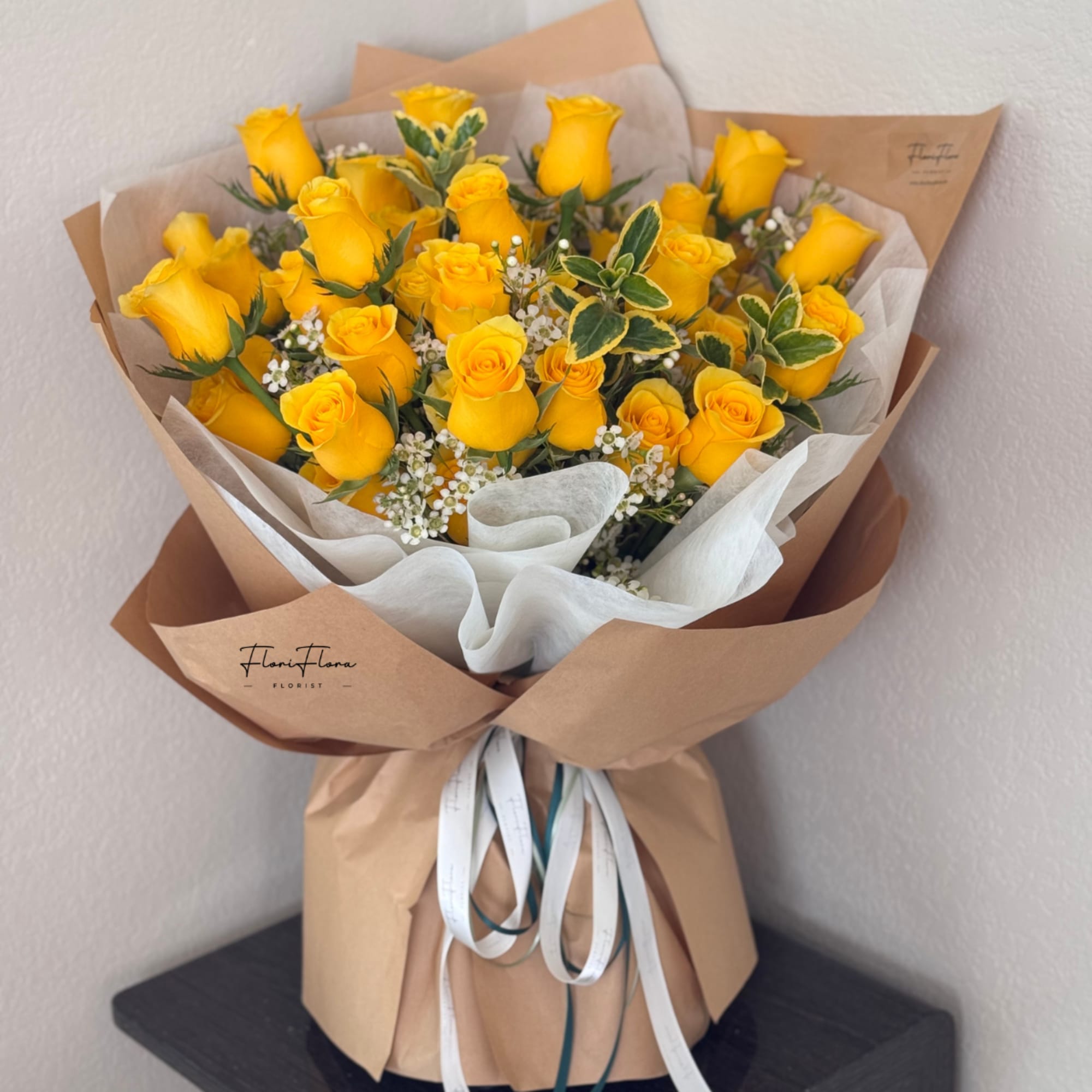 Bouquet of yellow roses wrapped in brown paper with white ribbon